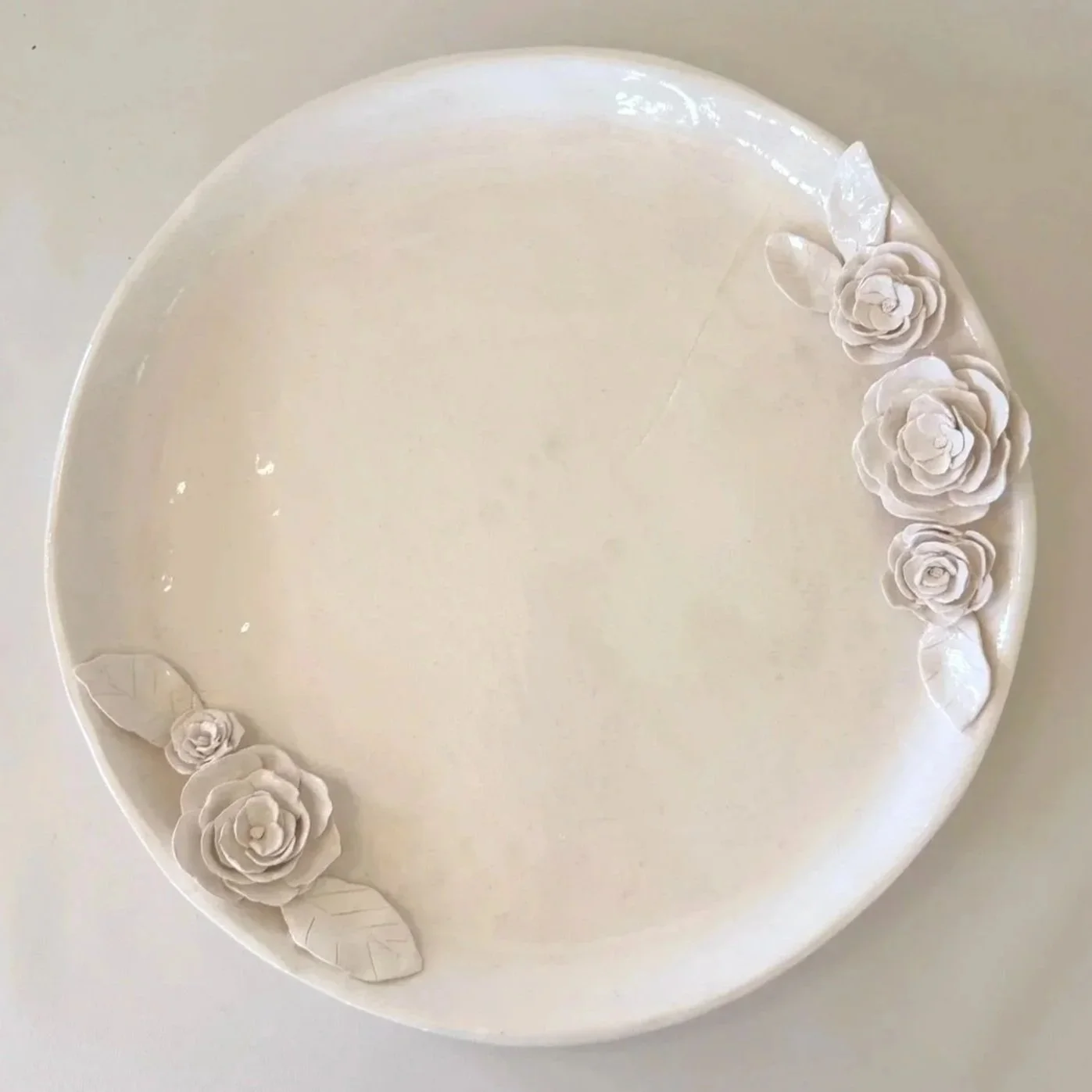 A white round cake decorated with white roses and leaves on the edge.