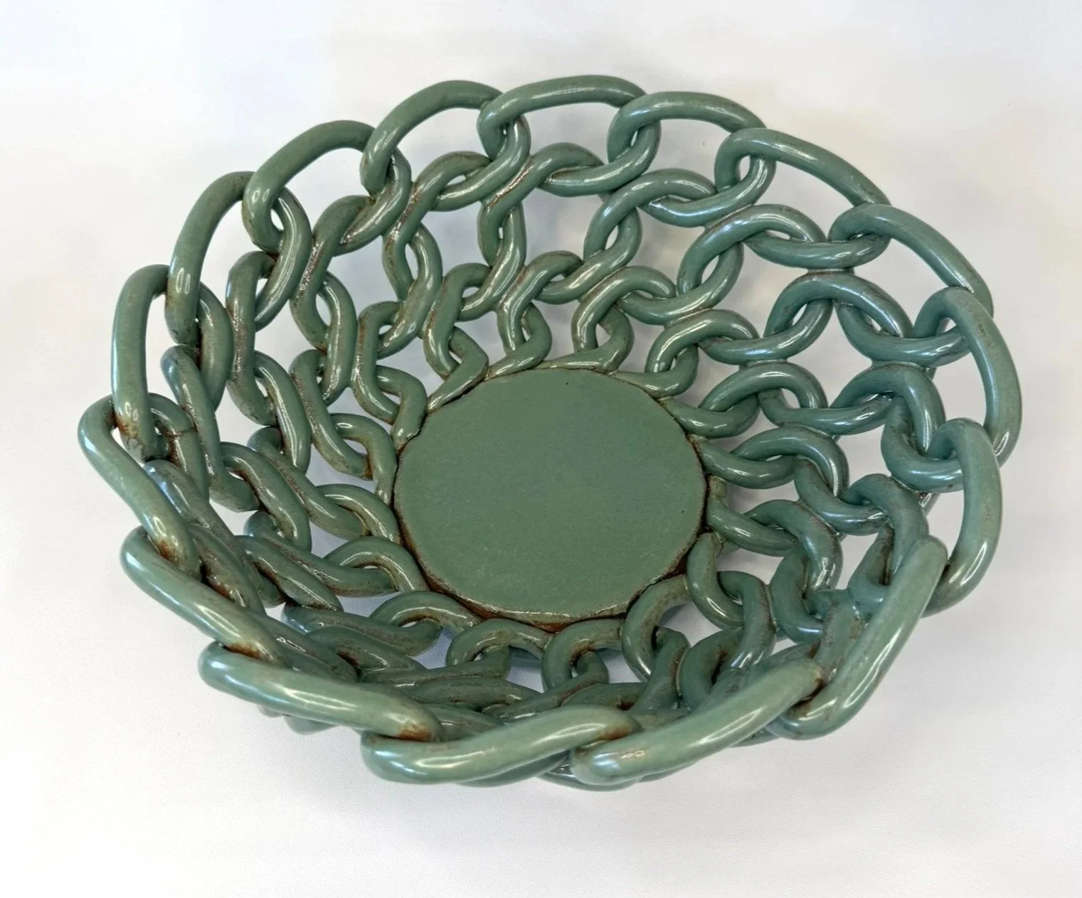 A round, flat, green ceramic object surrounded by a wire or chain intertwined in a circular pattern.