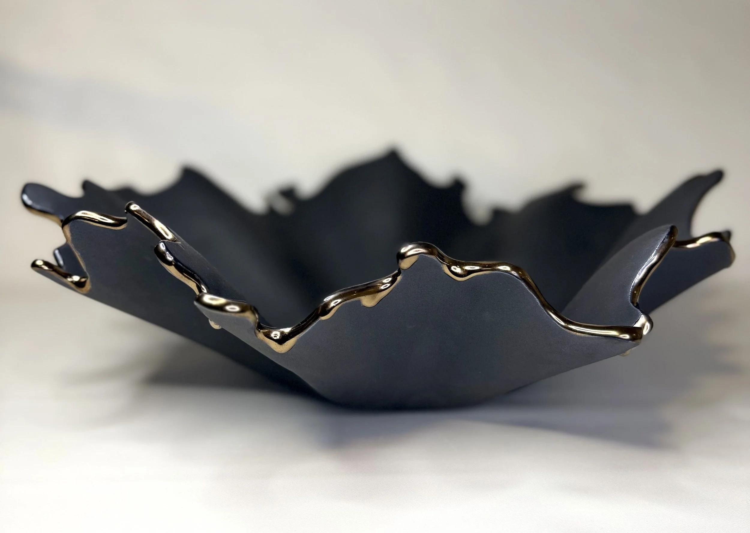 A close-up of a decorative bowl with a black matte finish and metallic accents along the edges, set against a plain background.