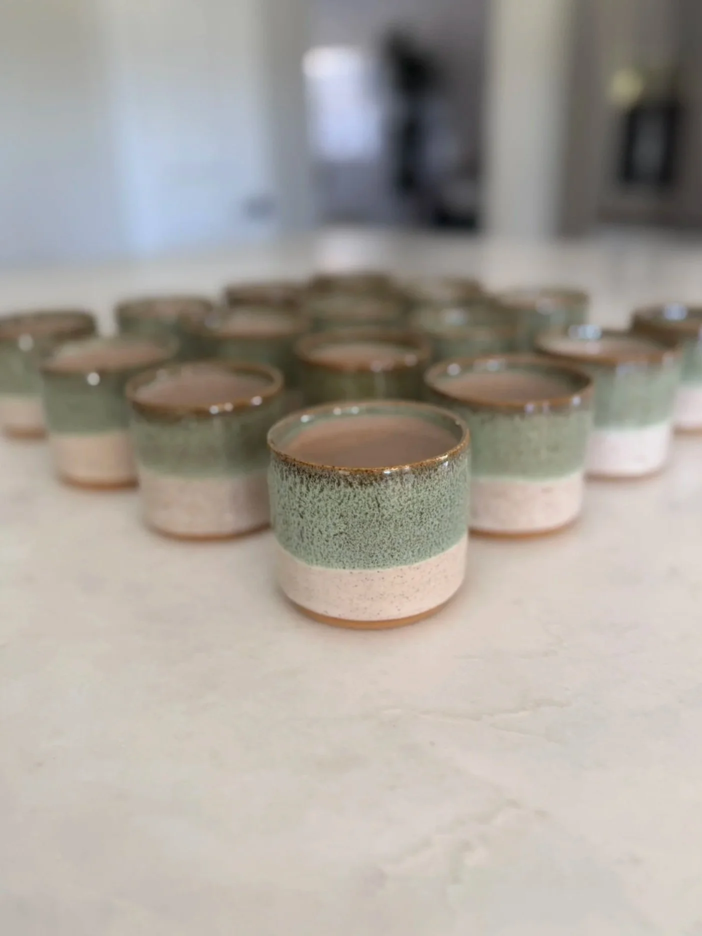 Multiple small ceramic cups with a green and beige speckled glaze, arranged on a flat surface.