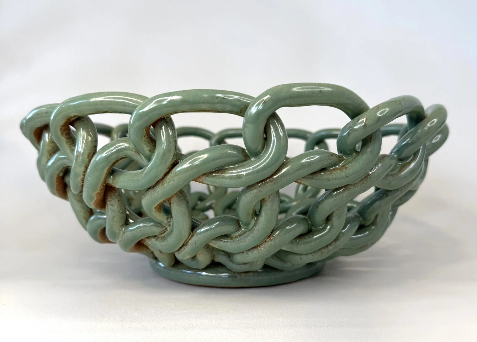 Green ceramic bowl with a chain link pattern on the outside, placed on a white surface with a plain white background.
