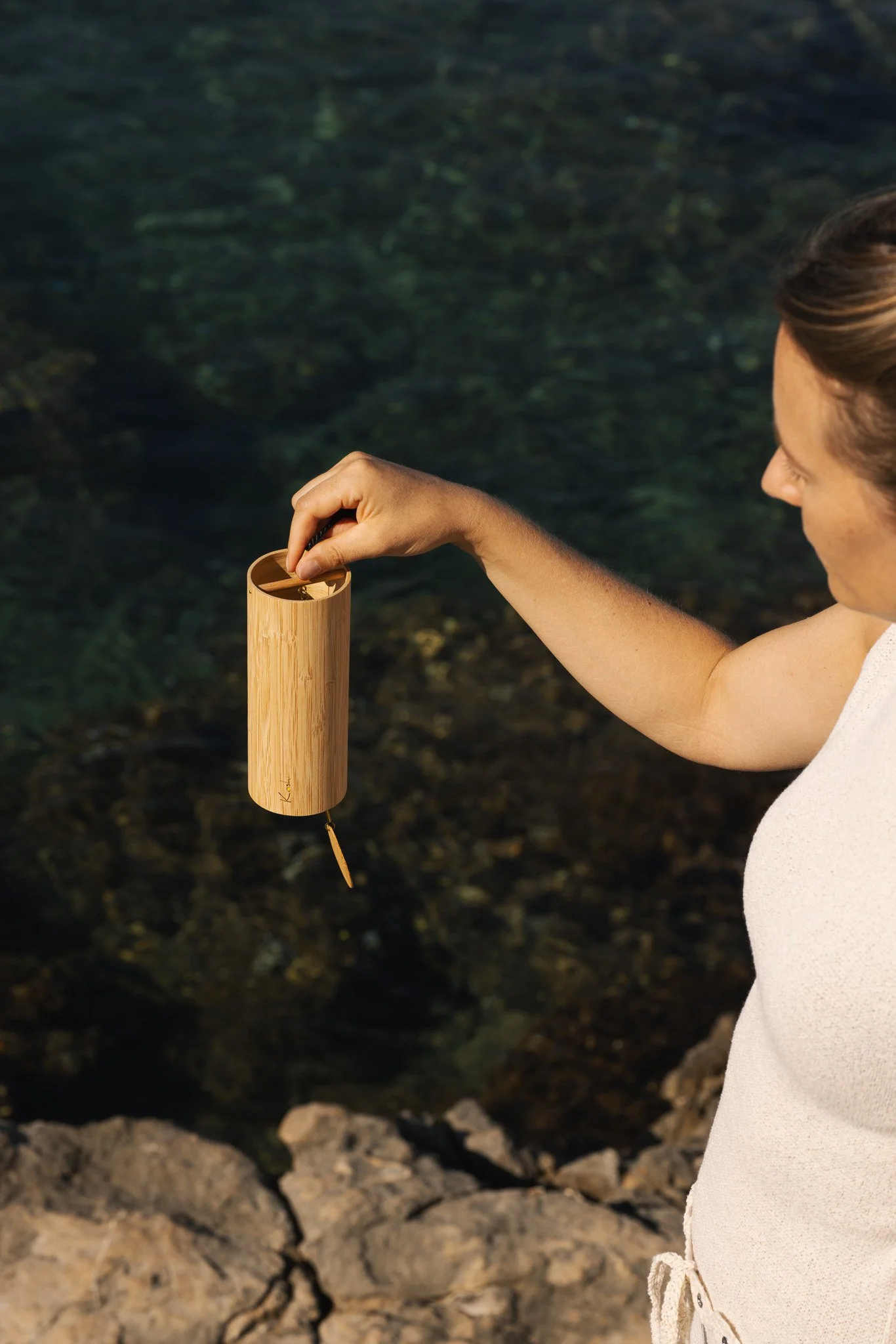Mujer sosteniendo un carillón cilíndrico de madera sobre el mar, Sonnenbaum, 2026
