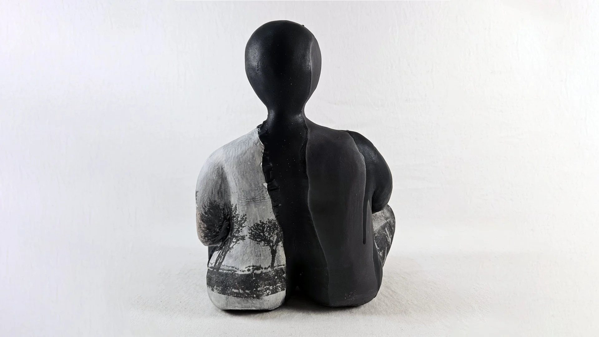 A sculpture of a human figure with divided halves, one side painted black and the other side featuring a landscape scene with trees in black and white.