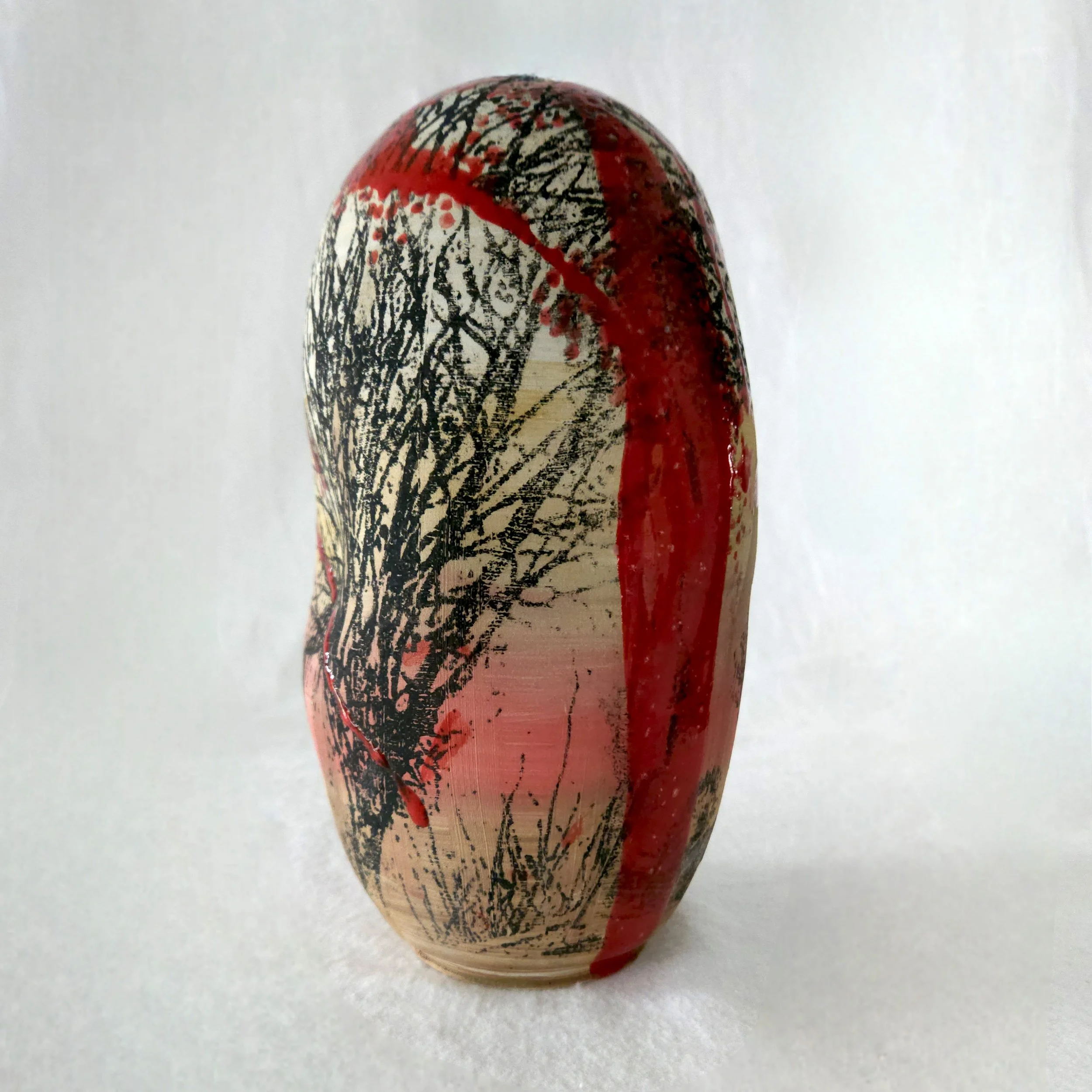 Decorative oval-shaped glass sculpture with black tree branch silhouettes and red accents.