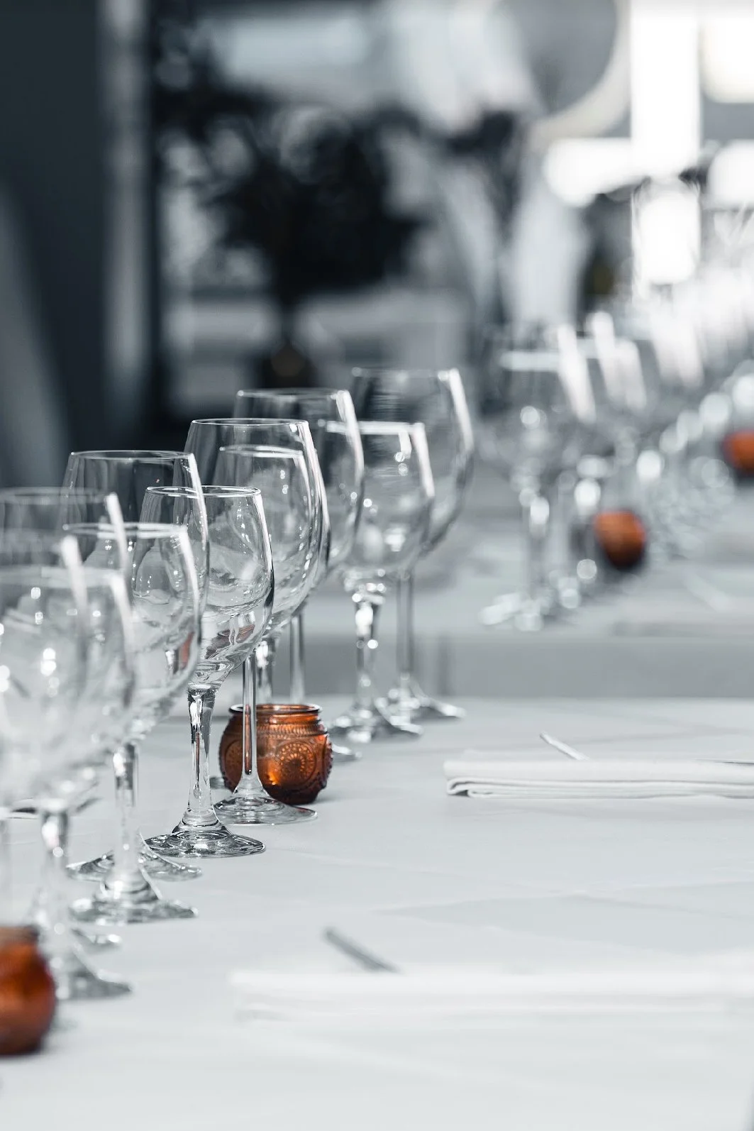 Empty wine glasses arranged on a table with white tablecloth, decorated with small amber candle holders, set for a formal event or dinner.