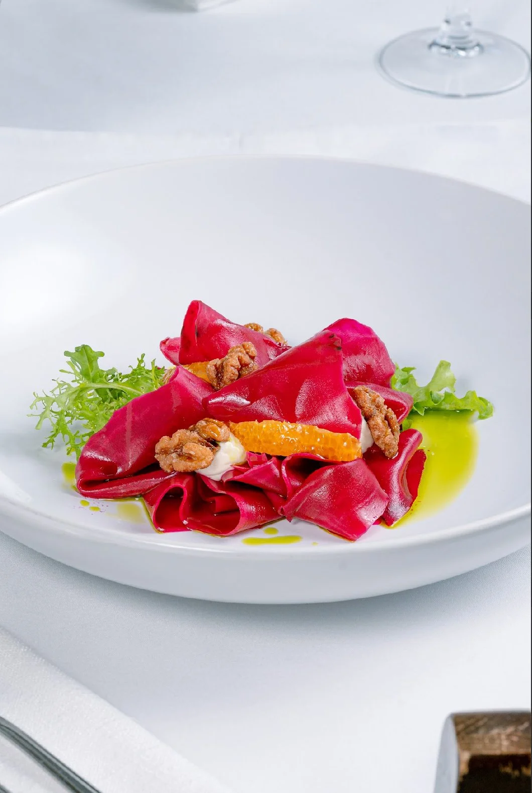 A white plate with pink pasta, garnished with orange slices, green lettuce leaves, and walnut pieces, drizzled with green oil.