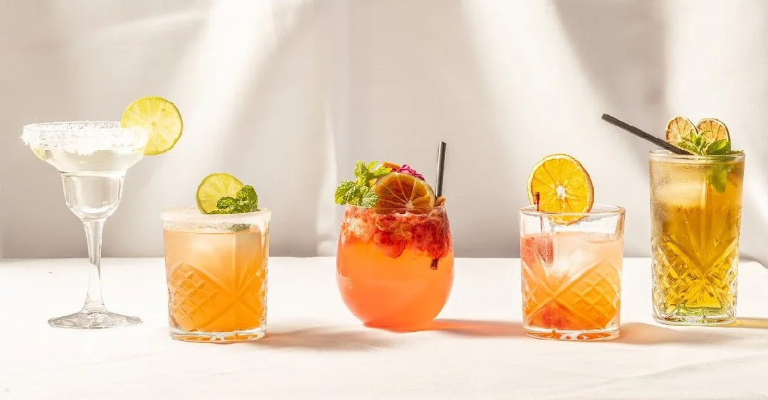 Five different cocktails with various garnishes on a white surface.