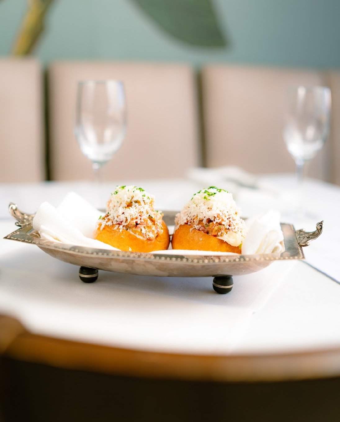 Two stuffed appetizers with a breadcrumb topping on a silver tray with white cloth at an elegant dining table.