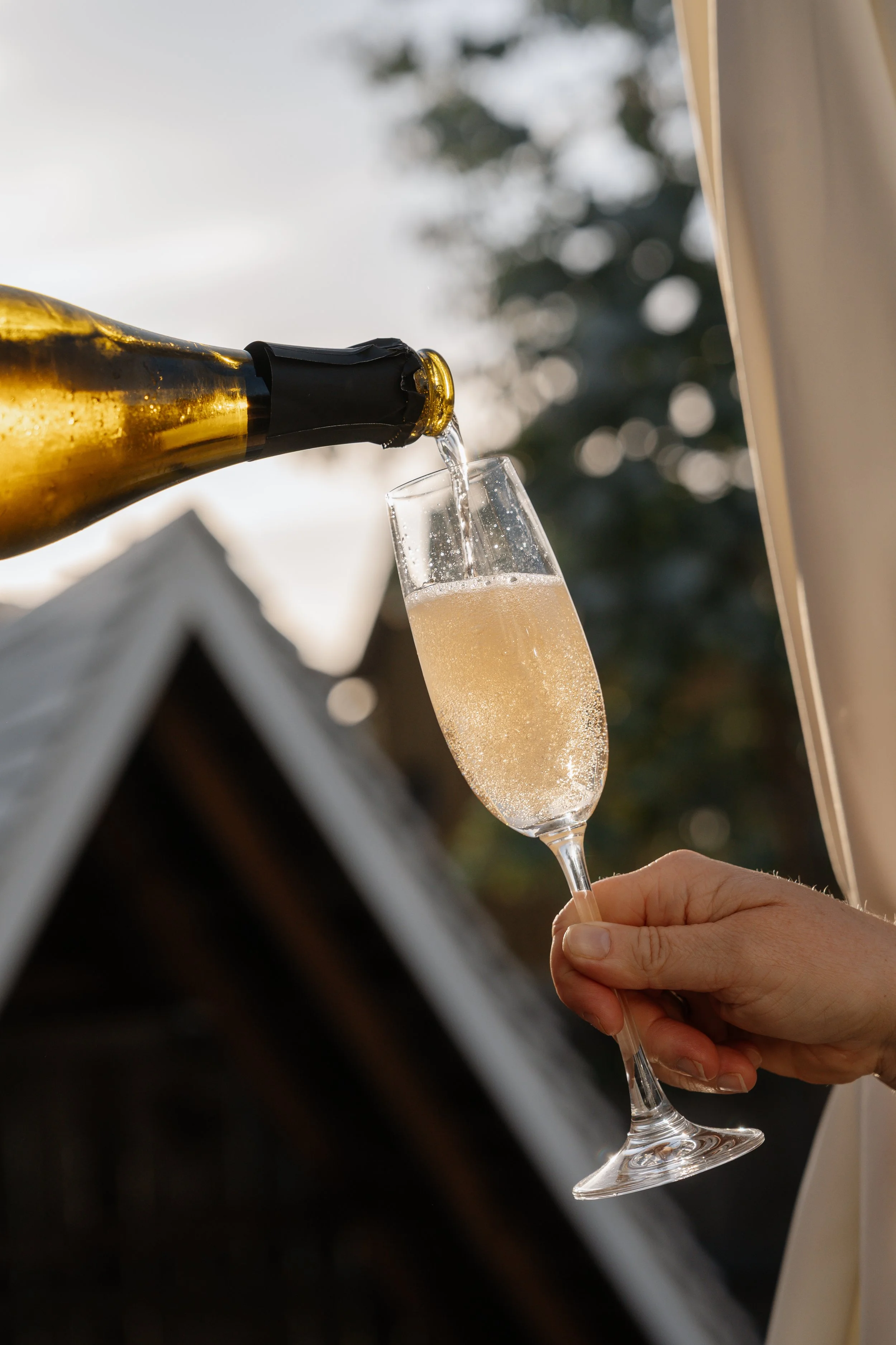 A hand holding a champagne flute catching a stream of champagne from a bottle.