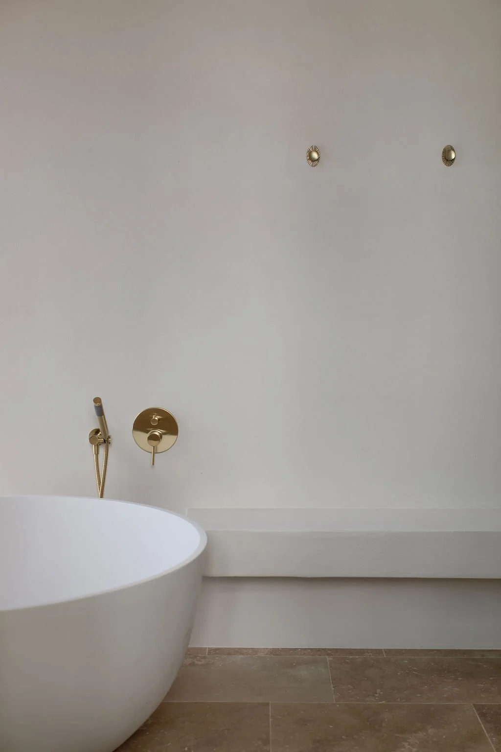 Part of a modern bathroom with a freestanding bathtub, gold wall fixtures, and a textured tile floor.