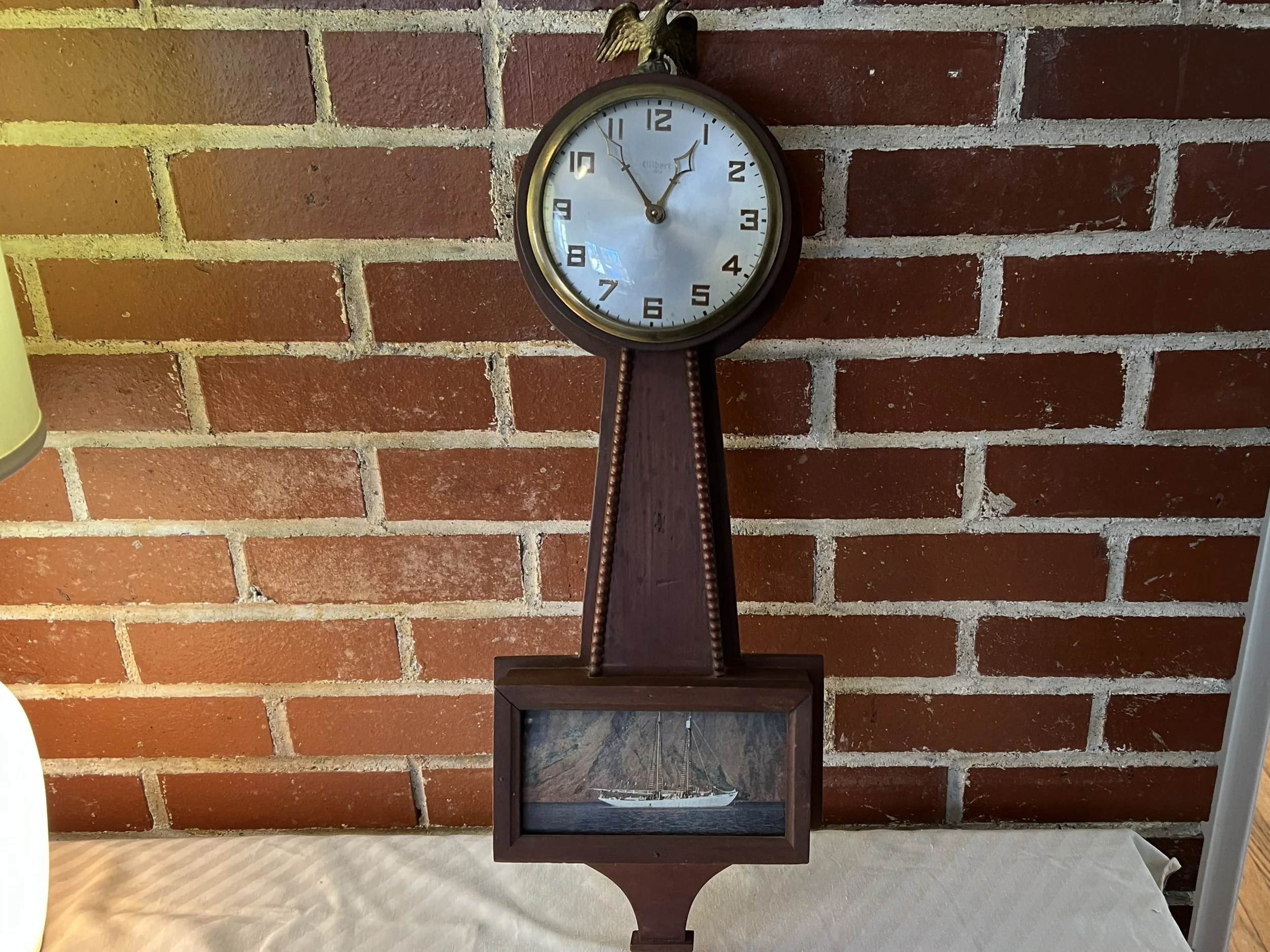 Vintage Gilbert Banjo Wall Clock featuring an 8-day key-wind movement and a decorated lower panel. 
Brand: Gilbert Clock Company, founded in Winchester, Connecticut. 
Design: These timepieces are known as "banjo" clocks due to their case shape, which