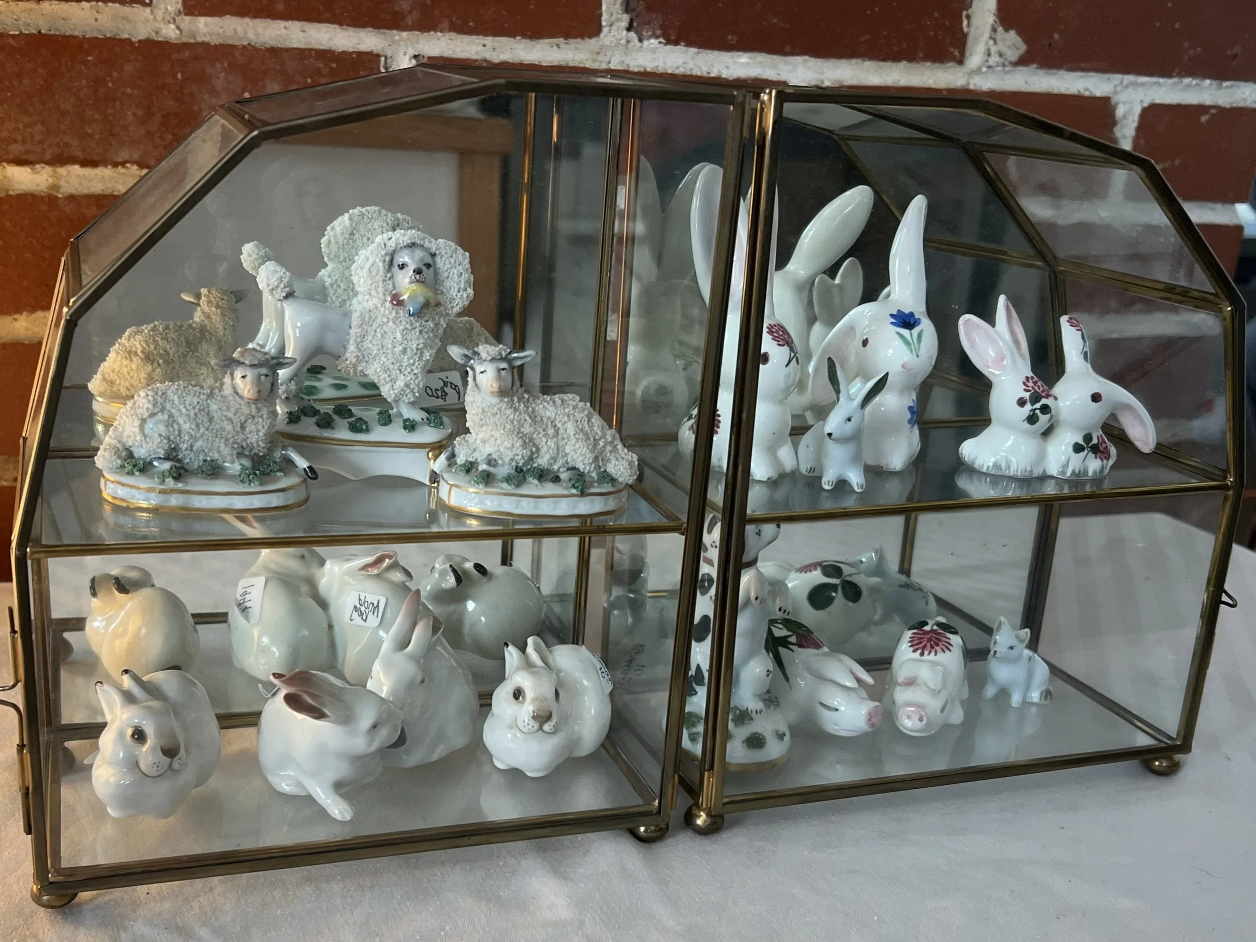 Glass display case with porcelain rabbit and sheep figurines, some with floral designs, and a ceramic dog figurine among the sheep.