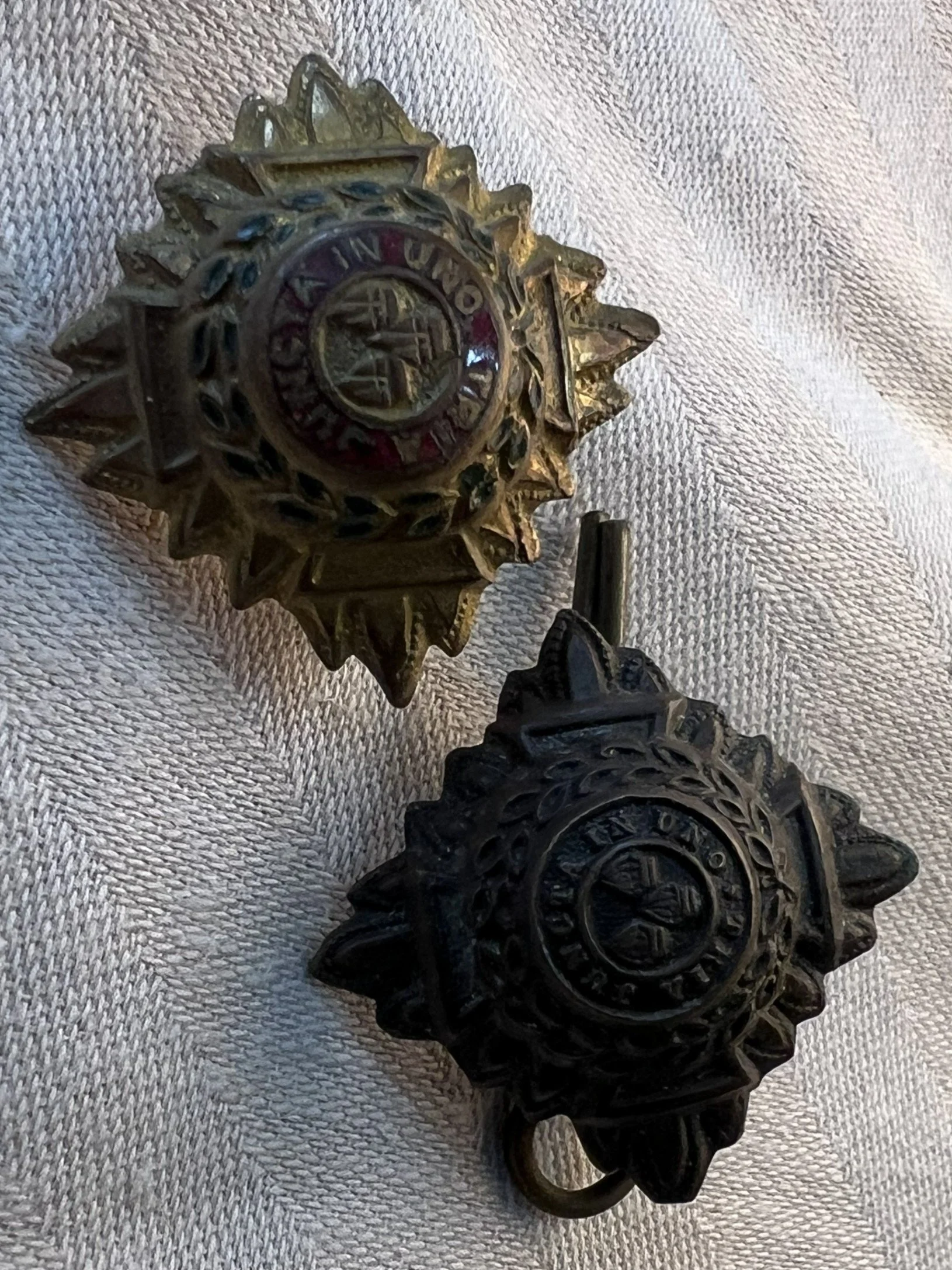 Two Soviet military badges with star shapes and inscriptions, one in gold color and the other in black, placed on a textured fabric background.