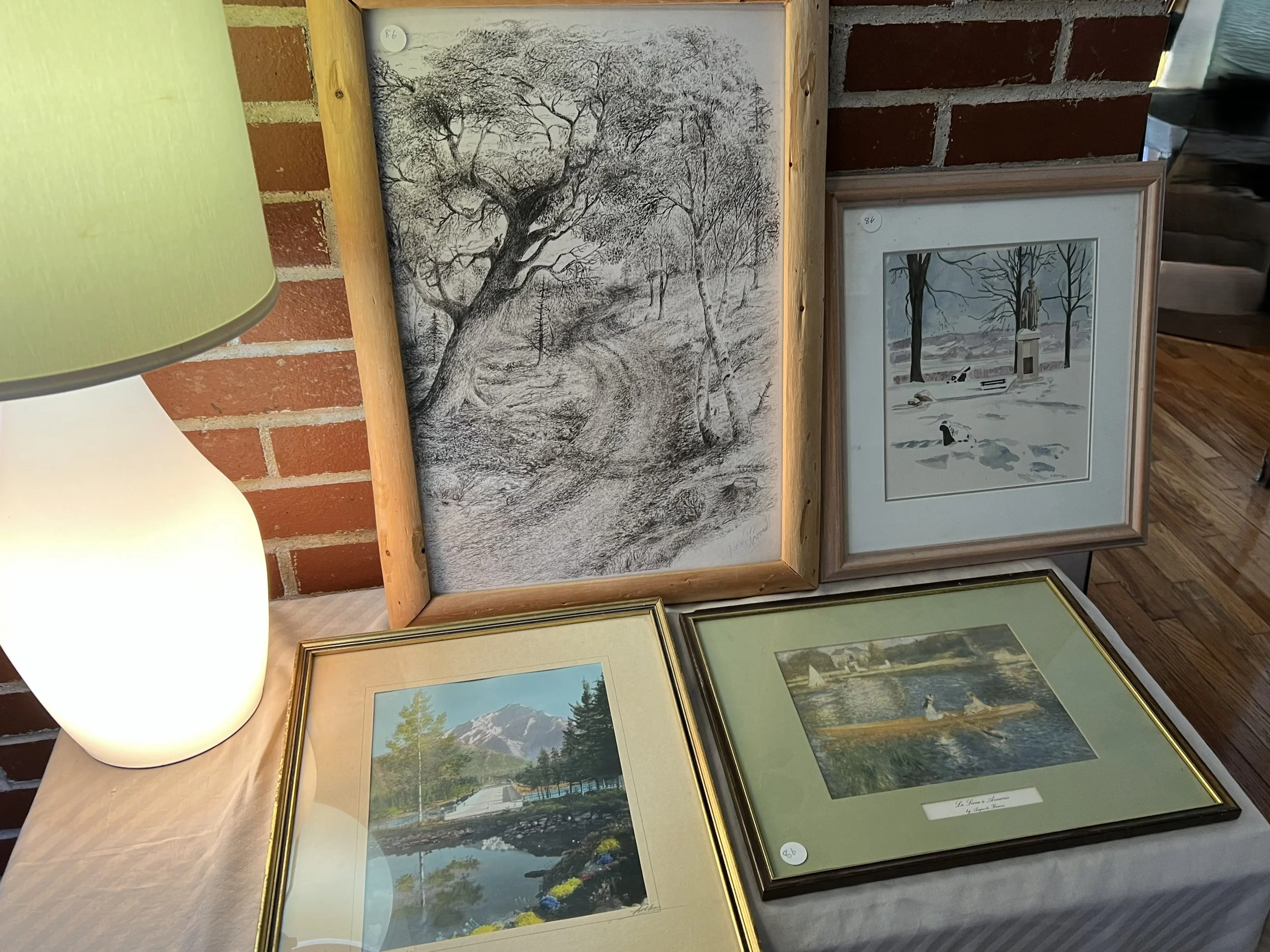 A display of four framed art prints, including a black and white landscape, a colored landscape, and a black and white scene with ducks in snow,