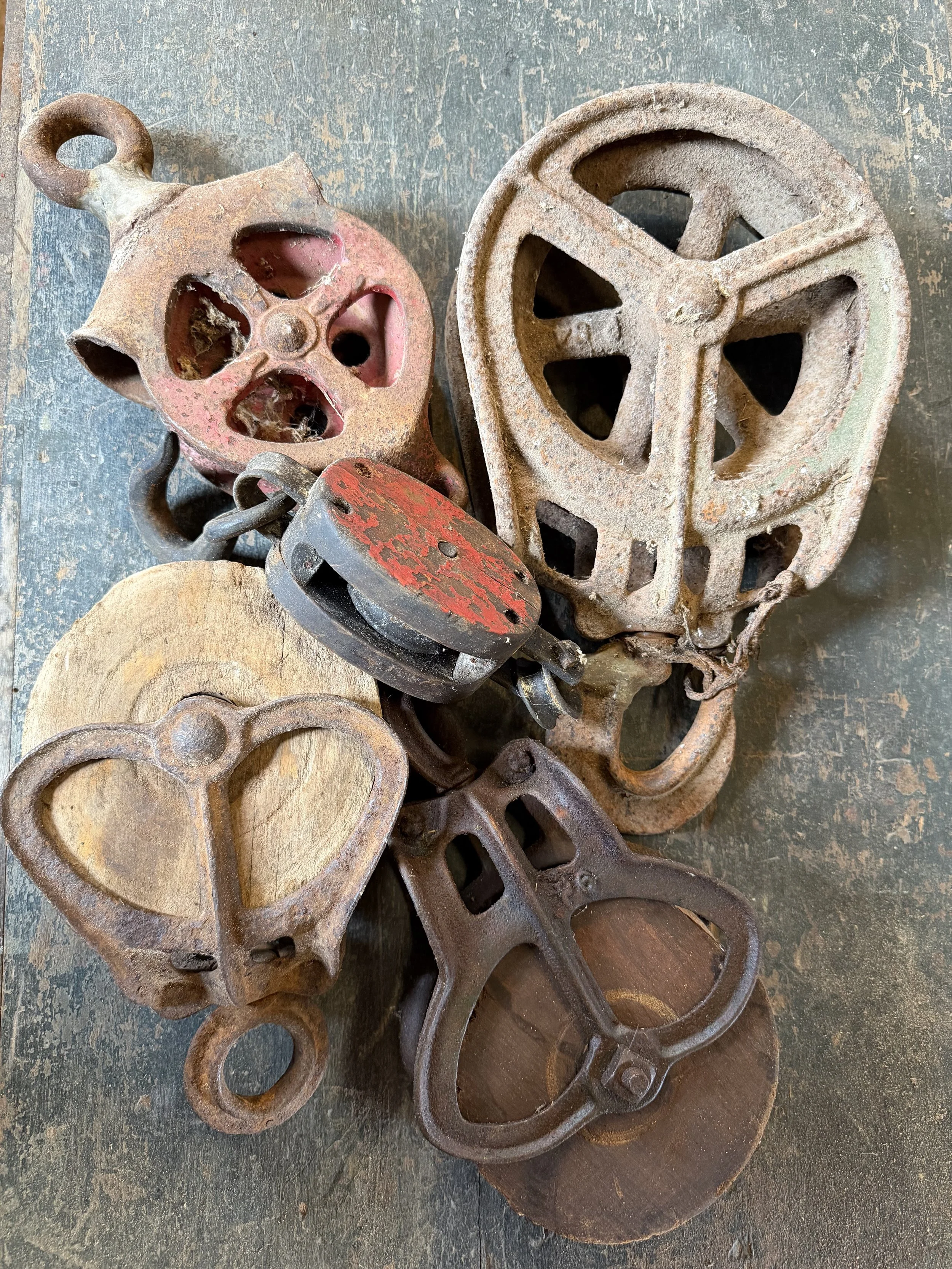 A collection of vintage metal pulleys, a rusty chain, a small wooden wood, and a metal trident.
