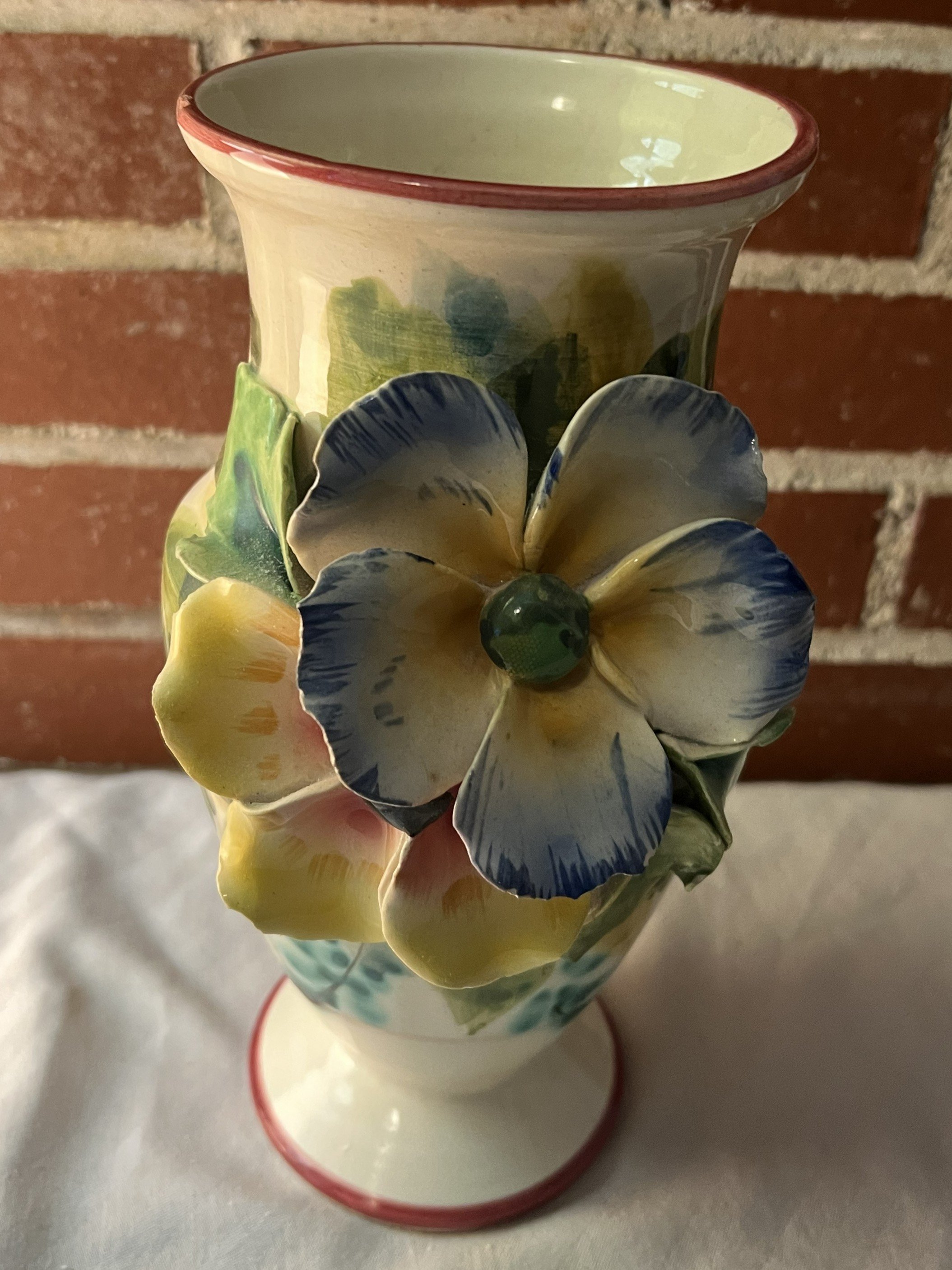 A decorative ceramic vase with large, three-dimensional, painted flowers attached to the surface. 