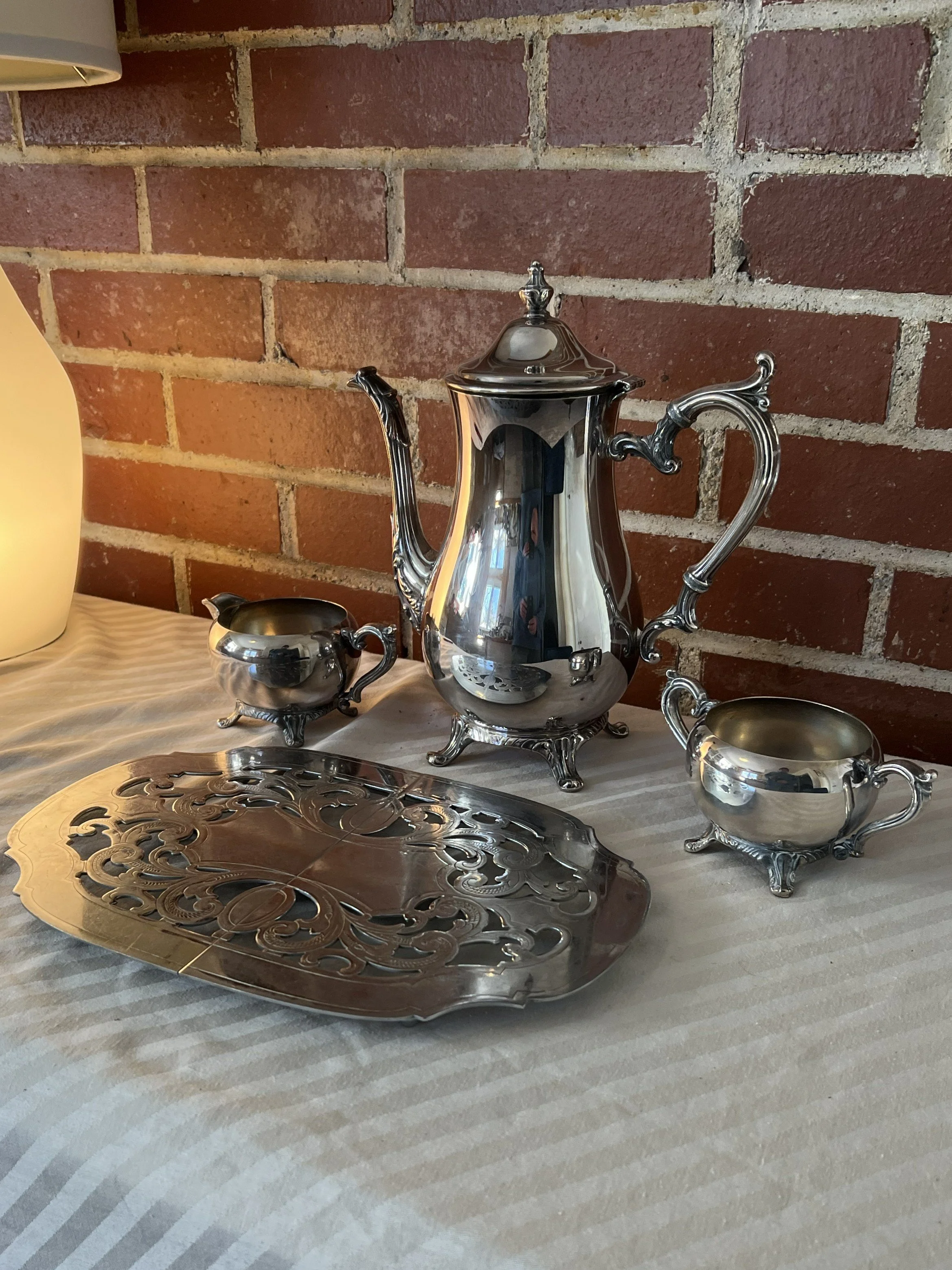 A polished silver tea set, including a teapot, sugar bowl, creamer, and a trivet