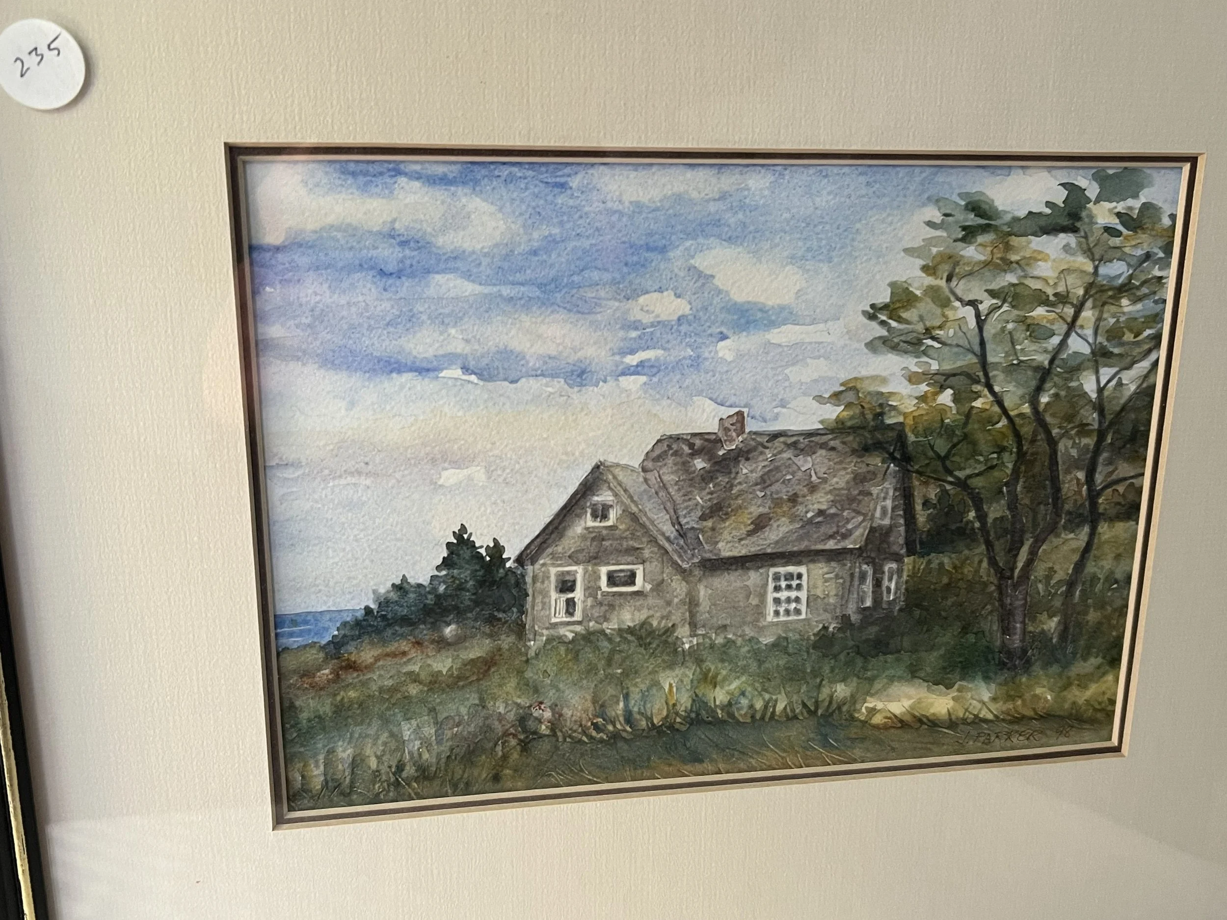 Watercolor painting of a house with a steep roof, surrounded by trees and bushes, under a partly cloudy sky.