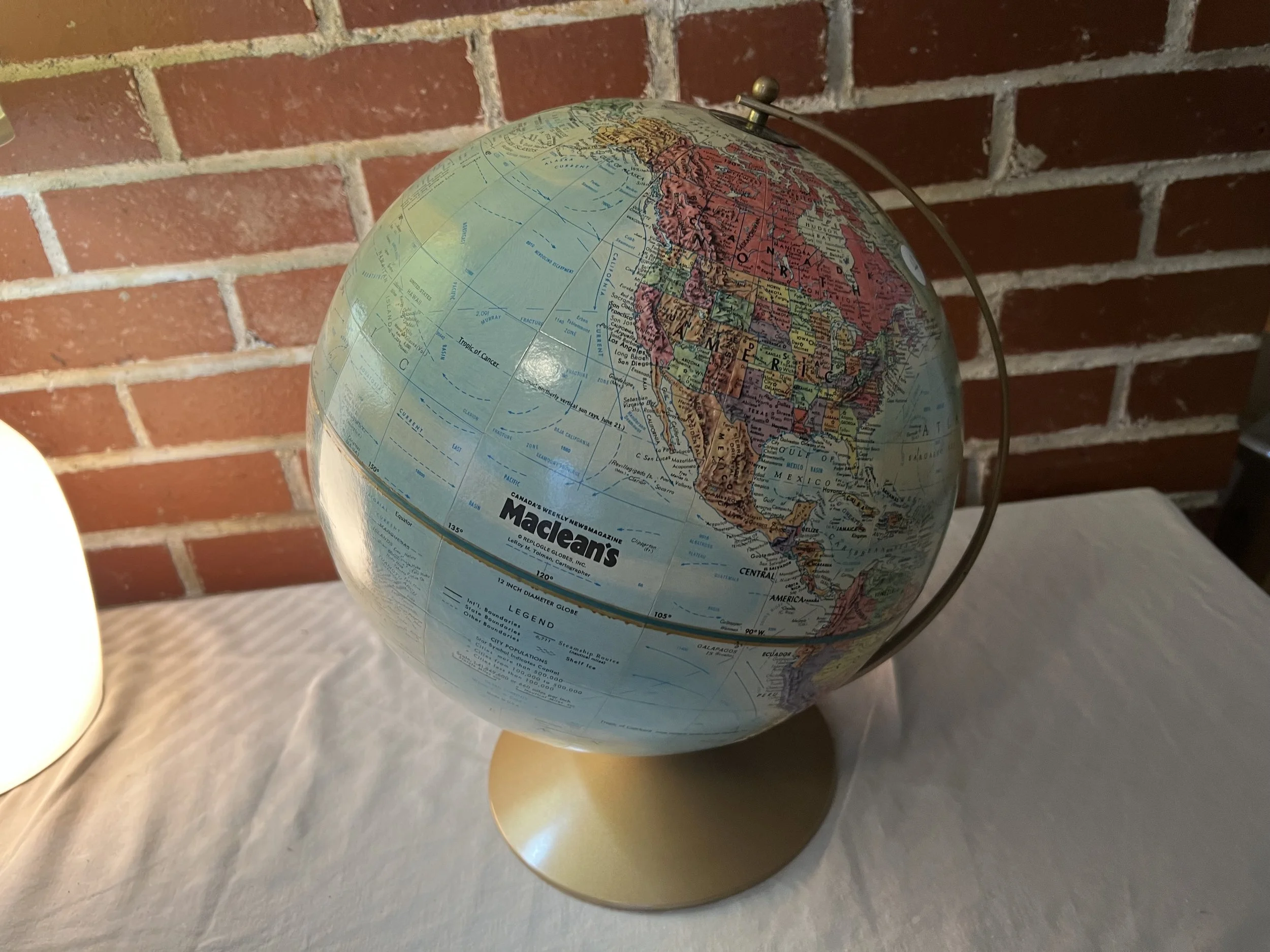 A vintage Replogle World Nation Series 12-inch tabletop globe specifically made for Maclean's Magazine. 
Features: Raised relief topography showing mountains and colorful political regions,. 
Design: Light blue oceans with a gold-colored matte metal 