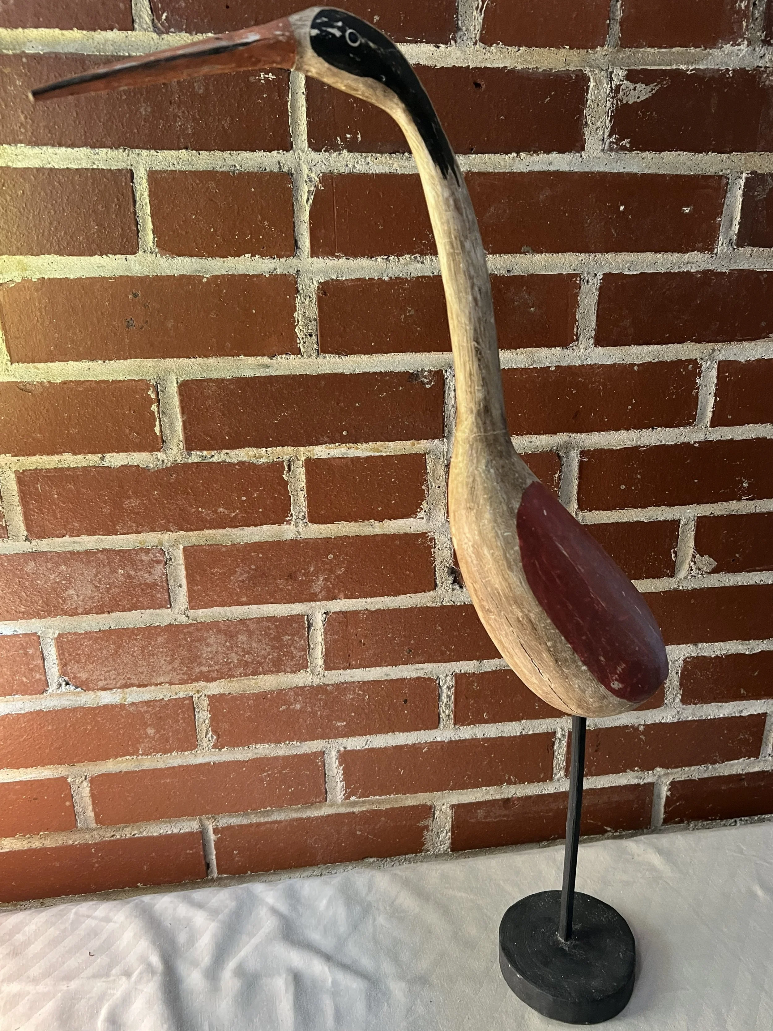 This item is a hand-carved wooden bird statue or decoy, likely representing a heron or shorebird, used for coastal home decor. 
Material: Carved wood with a painted finish and a metal stand. 
Dimensions: Typically measures around 15-16 inches in heig