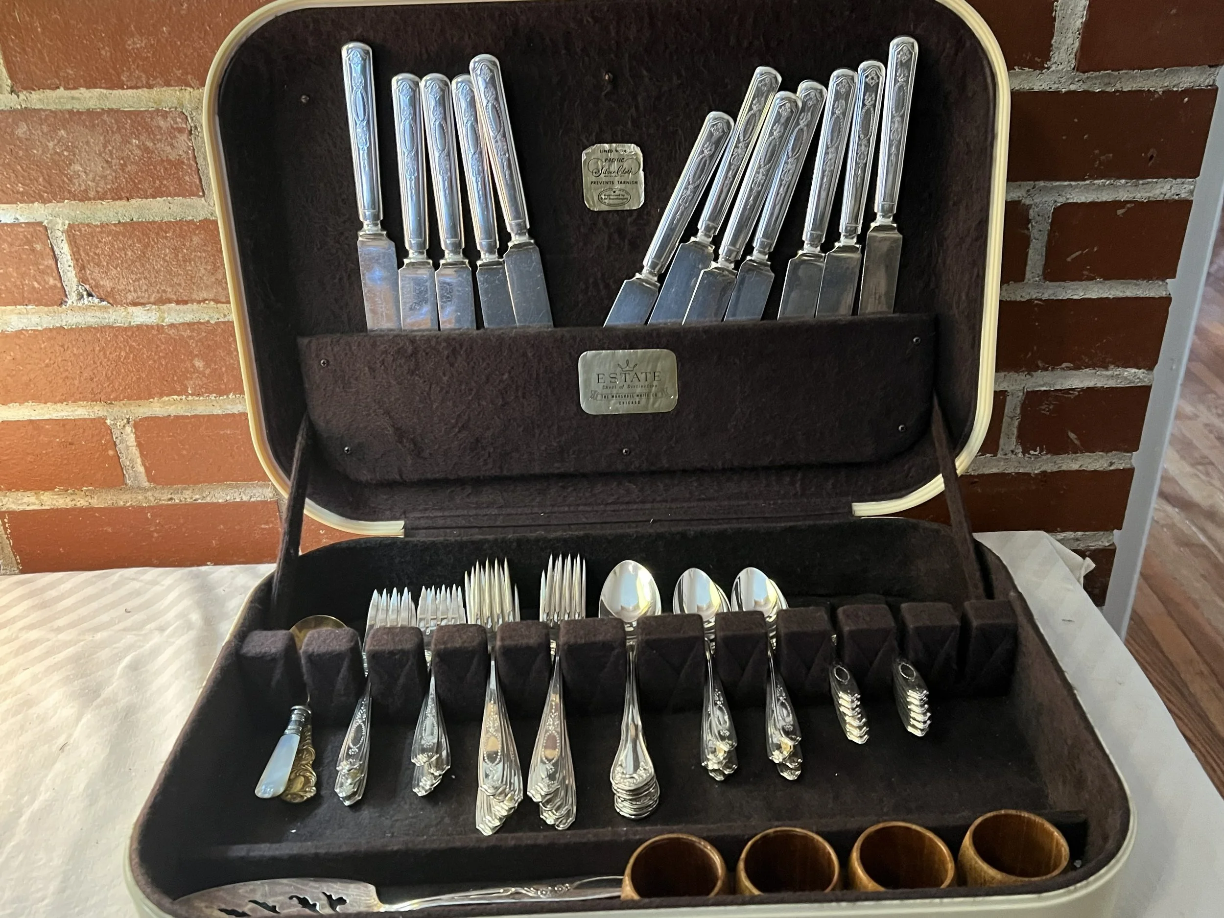 A vintage plastic and fabric case containing a set of silverware, including knives, forks, and spoons, with some wooden shot glasses.