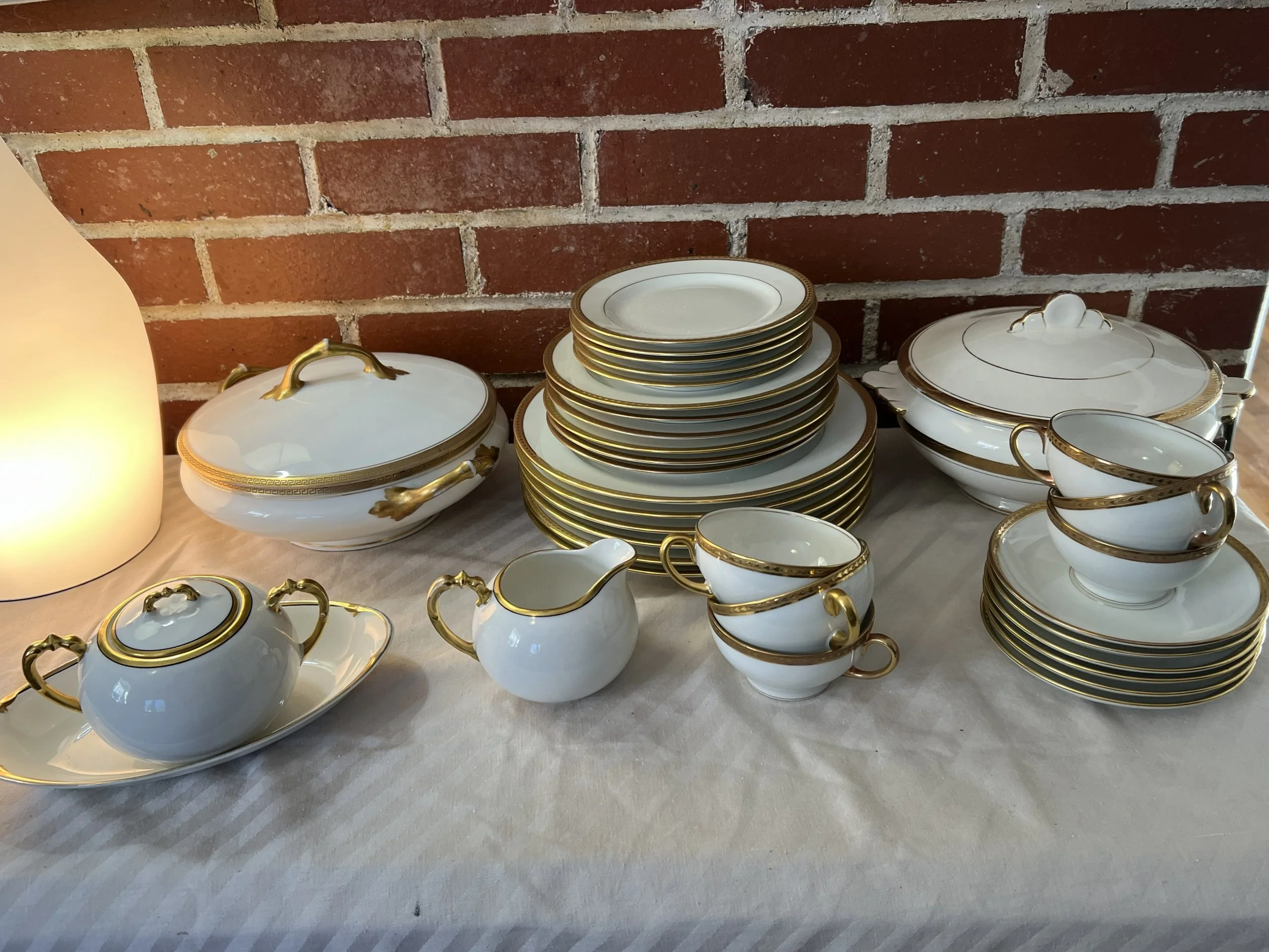 This vintage Coronet Limoges porcelain dinner service features a white glaze with simple gold rims and highlights. Limoges porcelain is known for being hard-paste, exceptionally durable, and translucent when held to the light. The set includes variou