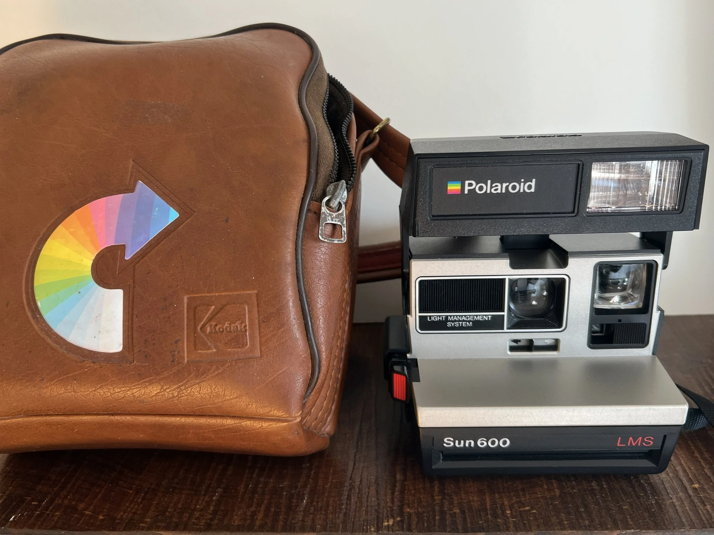 Vintage Kodak brown leather camera bag adorned with the iconic rainbow arrow logo. The bag is designed as a crossbody or shoulder carrying case and measures approximately 8 inches long. While branded by Kodak, these bags are often used to store and t