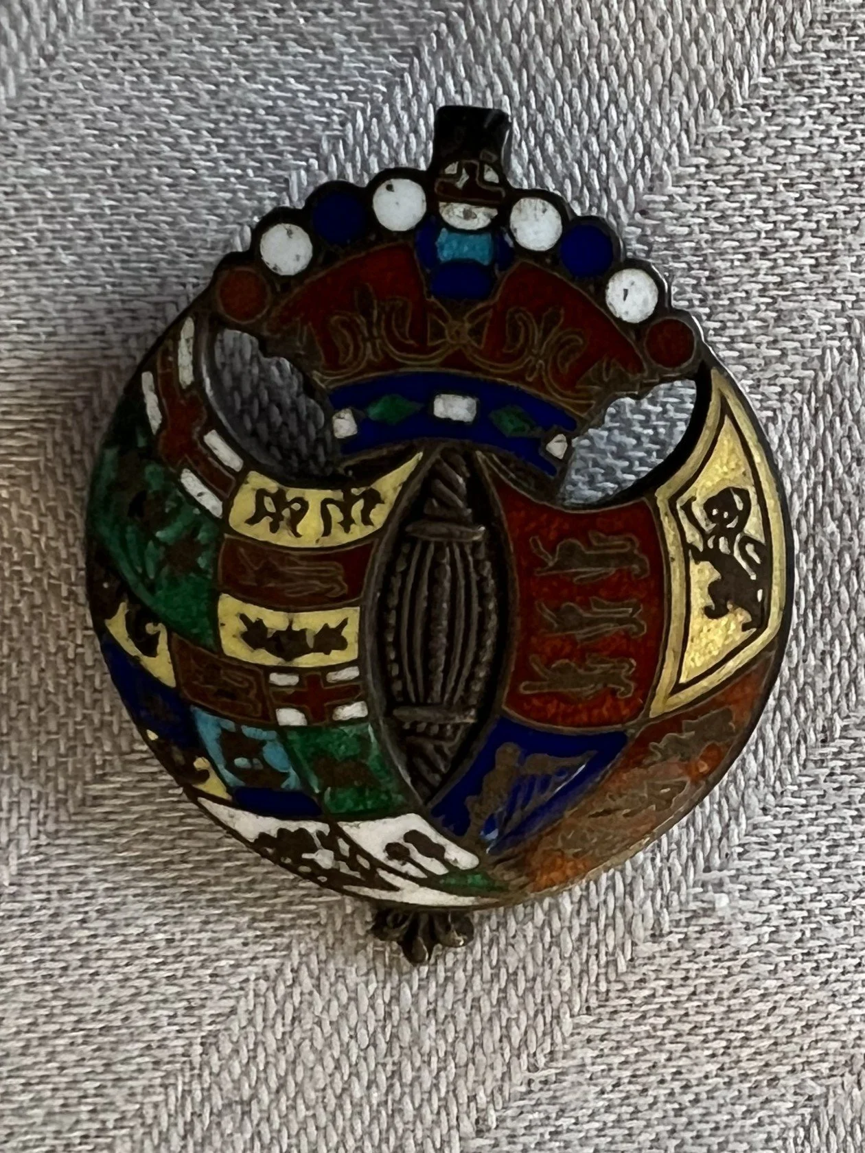 Colorful stained glass pin featuring a British royal crown, a ship, and heraldic shields on a fabric background.