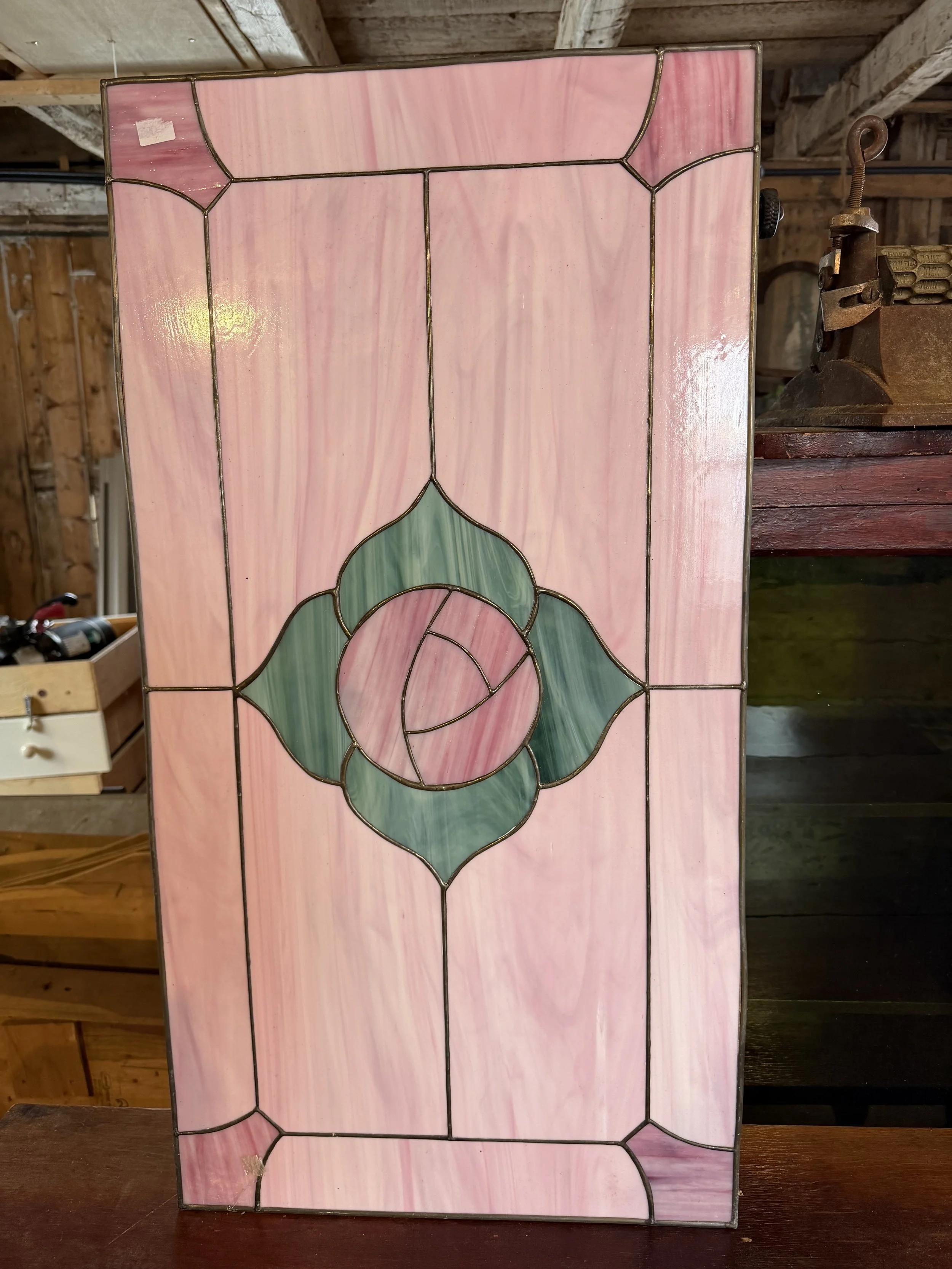 A stained glass window with pink and green glass pieces forming a floral pattern, framed with black metal outlines.