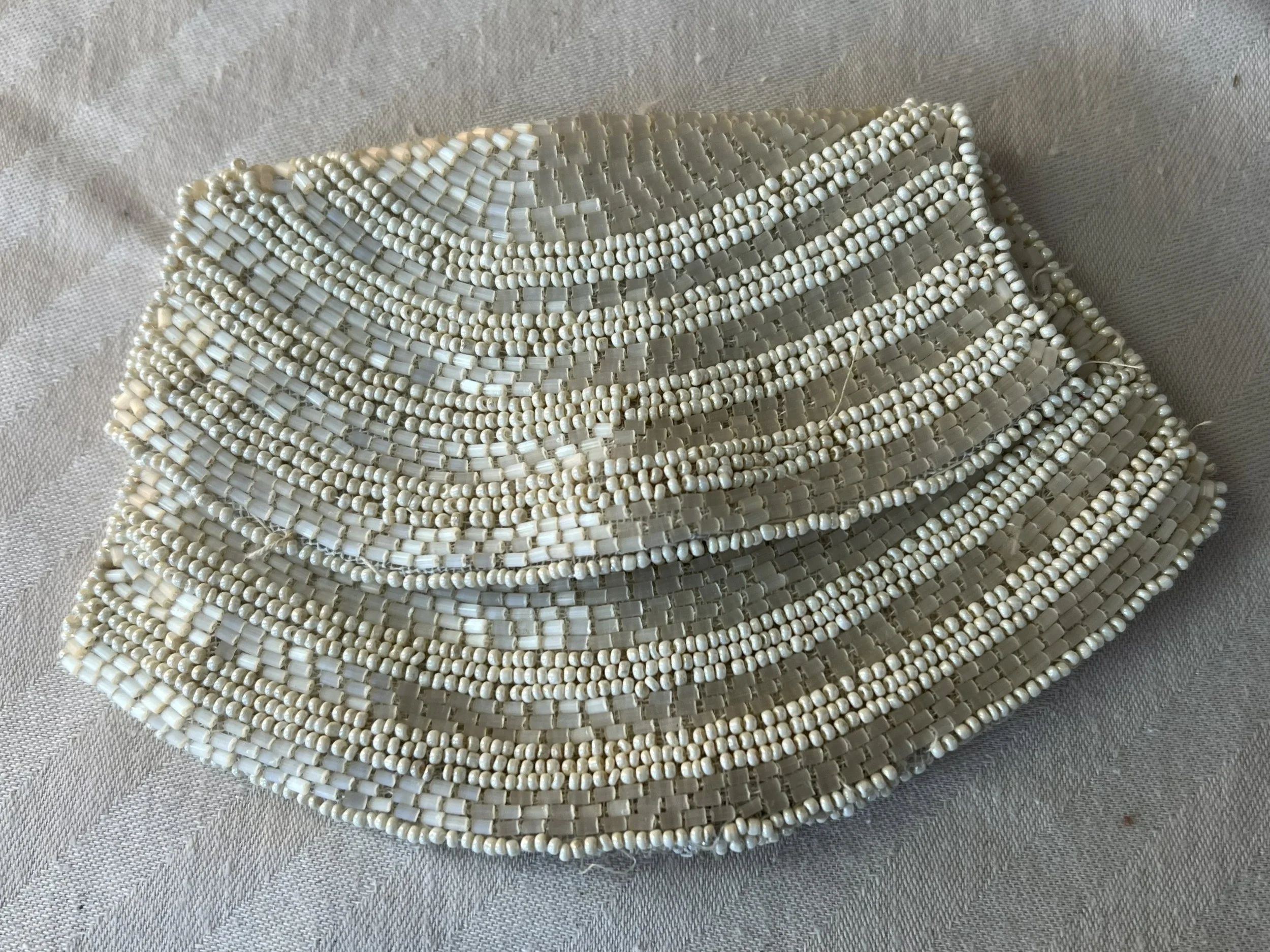 A beaded wedding clutch purse made of white and off-white beads, arranged in horizontal stripes of various sizes and shapes.
