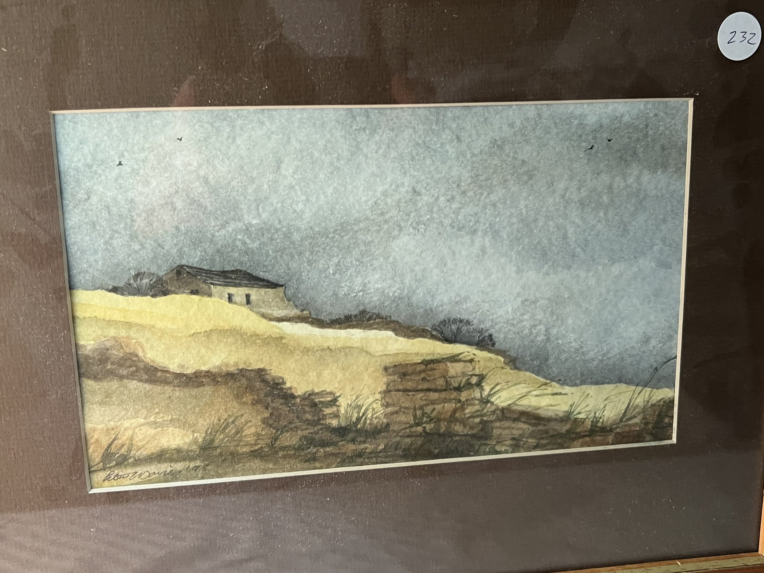 Watercolor painting of a hill with dry grass and a small house or barn at the top, under a cloudy sky, signed by the artist at the bottom left.