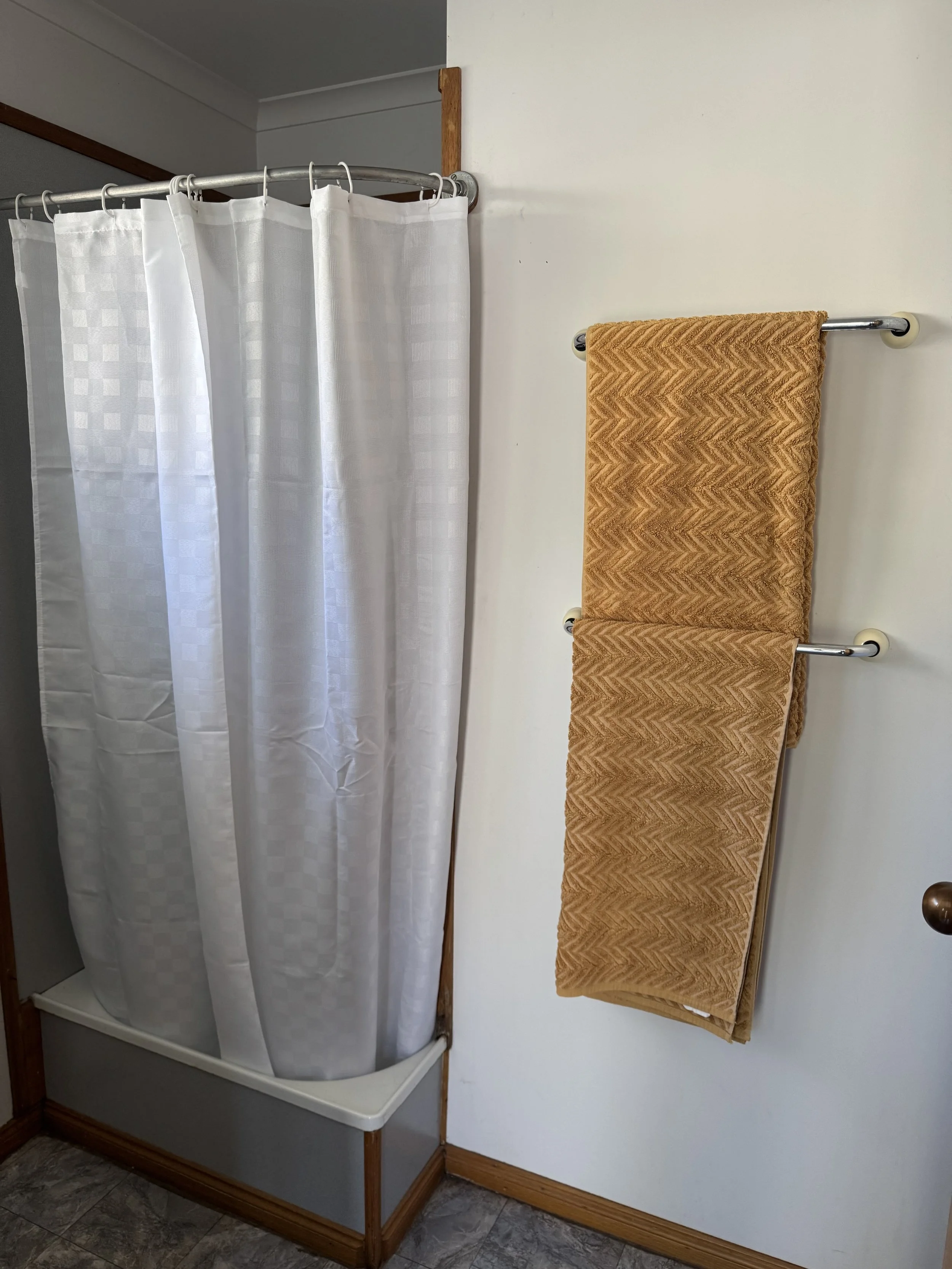 A bathroom with a white checkered shower curtain and two brown patterned towels hanging on a metal towel rack.