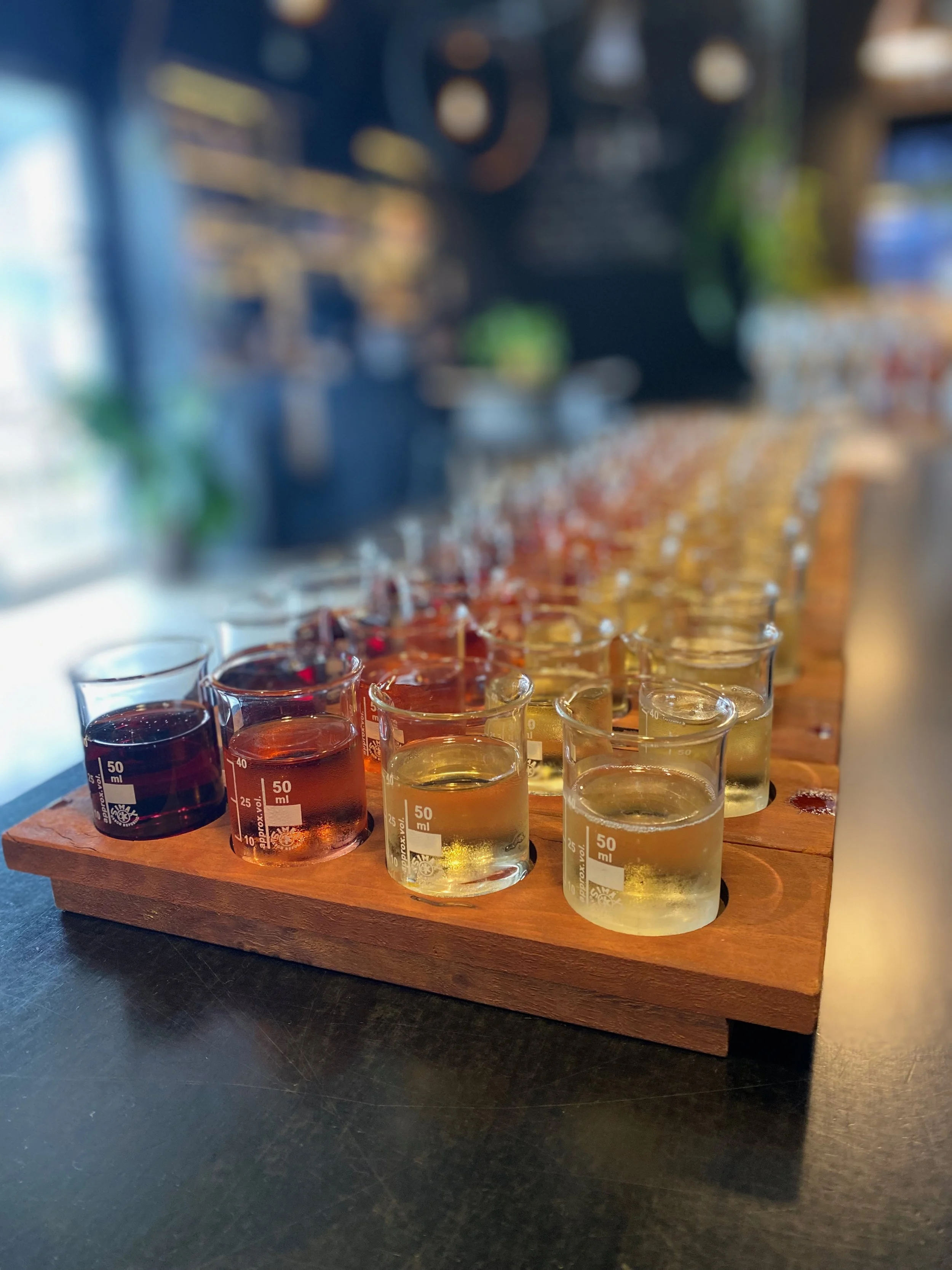 An assortment of small laboratory beakers filled with different colored liquids, placed on a wooden tray.