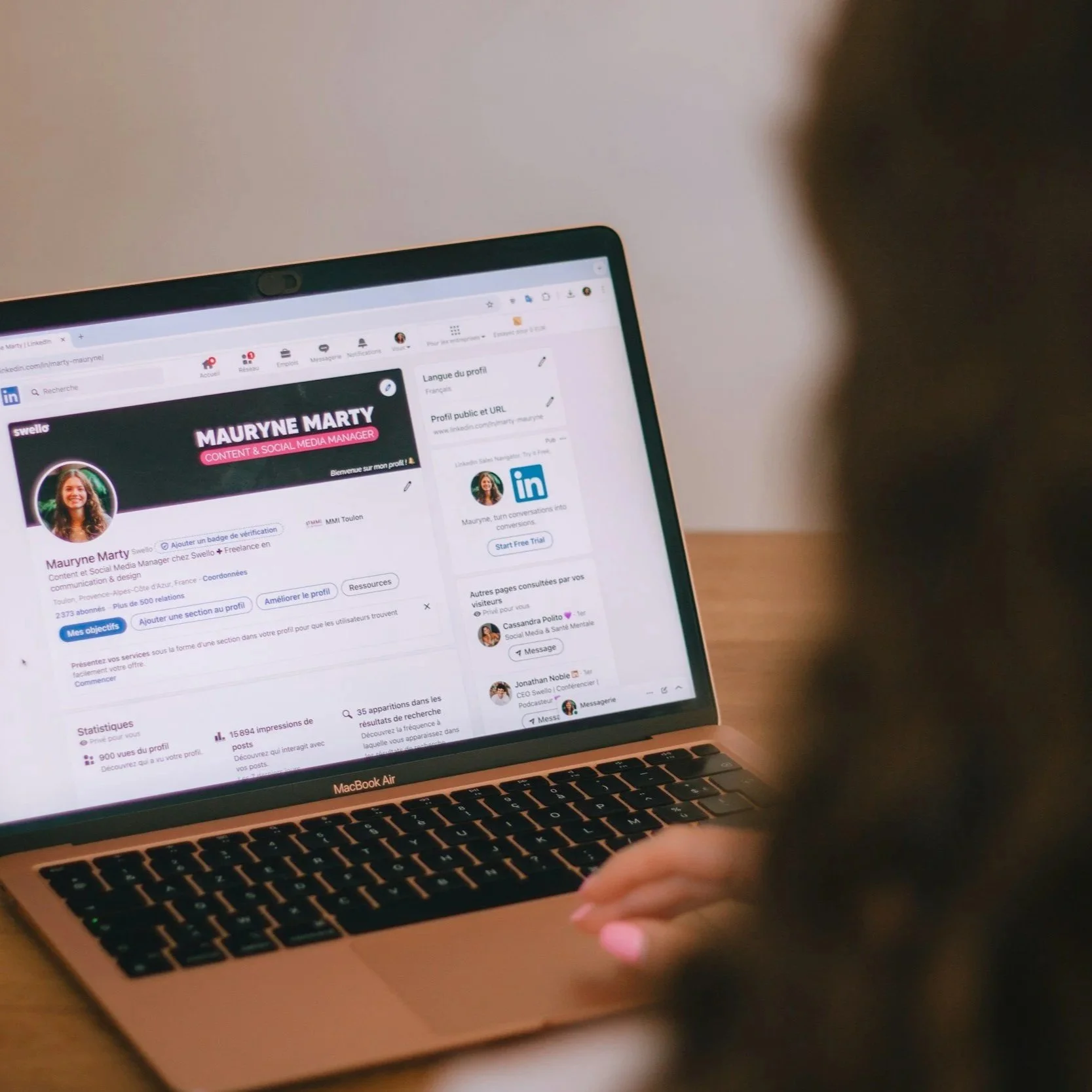 A person using a MacBook Air laptop displaying a LinkedIn profile of Mauryne Marty, a Content & Social Media Manager, with a blurred background.