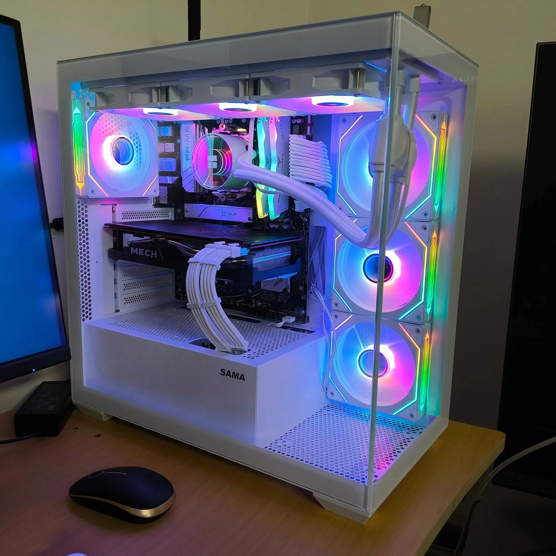A custom-built gaming computer with a white case, multiple RGB fans on the front and top, and RGB lighting inside visible through a transparent side panel, placed on a wooden desk near a computer monitor and mouse.