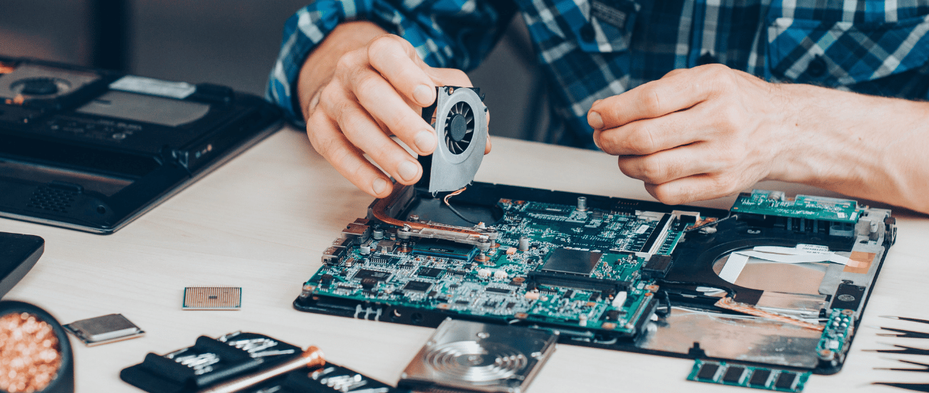 Person repairing a laptop by installing a cooling fan onto the motherboard.