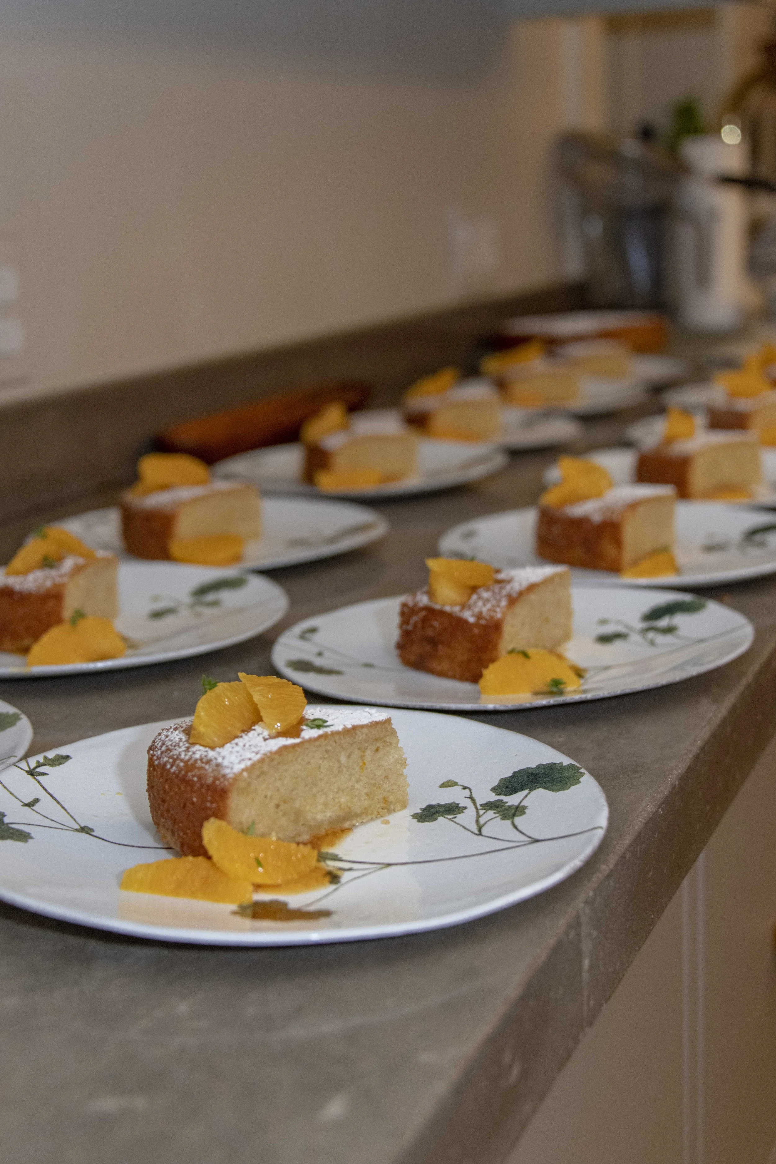 Multiple plates of sliced sponge cake topped with powdered sugar and garnished with peach slices, arranged on a countertop.