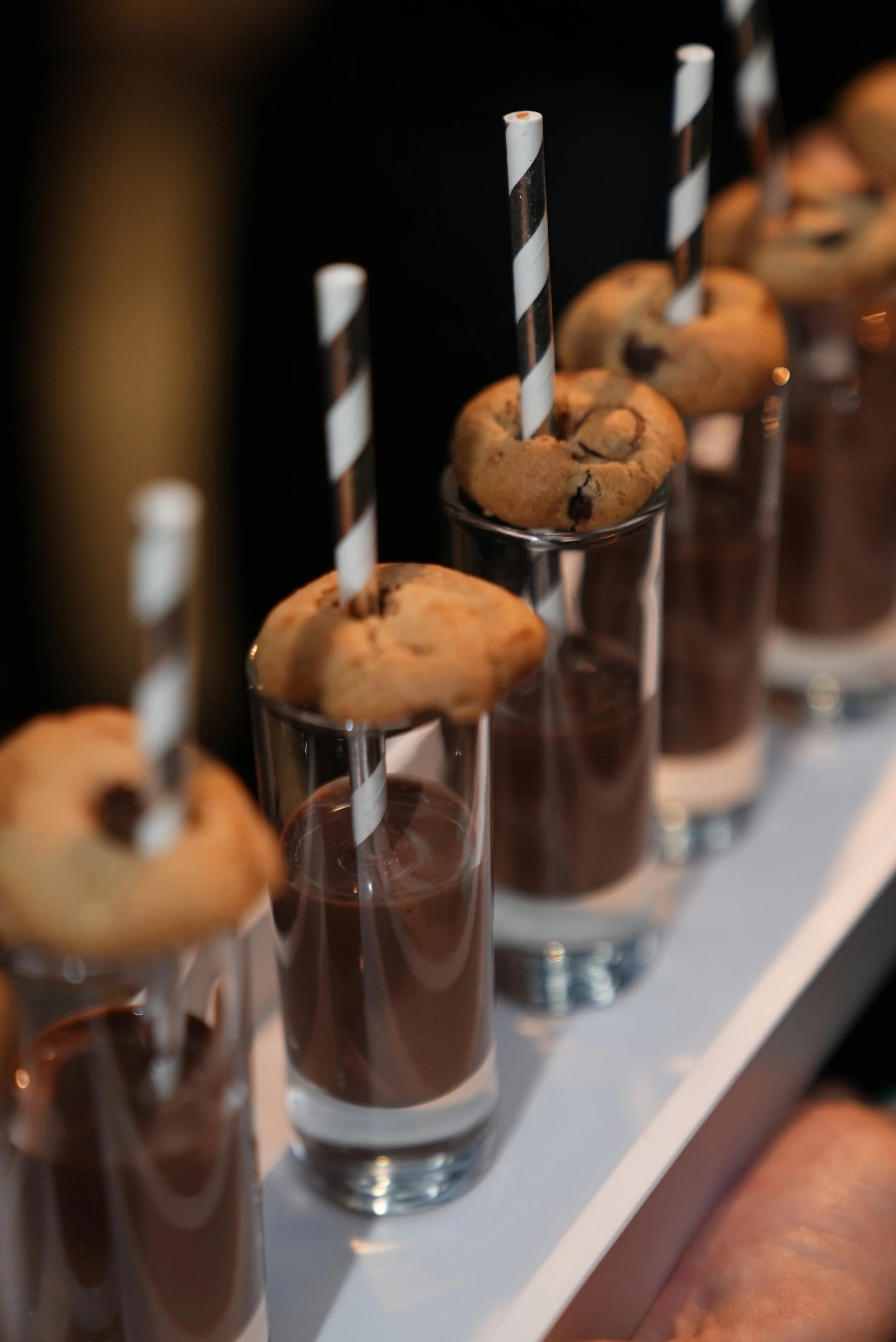 Chocolate drinks in tall glasses topped with chocolate chip cookies and black-and-white striped straws.