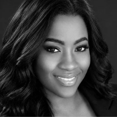 Black and white portrait of a smiling woman with wavy hair and makeup.