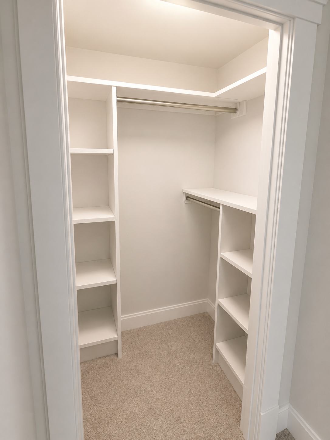 Empty white walk-in closet with shelves and hanging rods, beige carpeted floor.