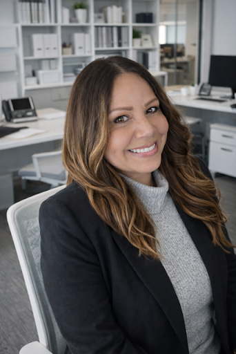 Melissa Jimenez smiling in an office environment, wearing a black blazer and gray sweater.