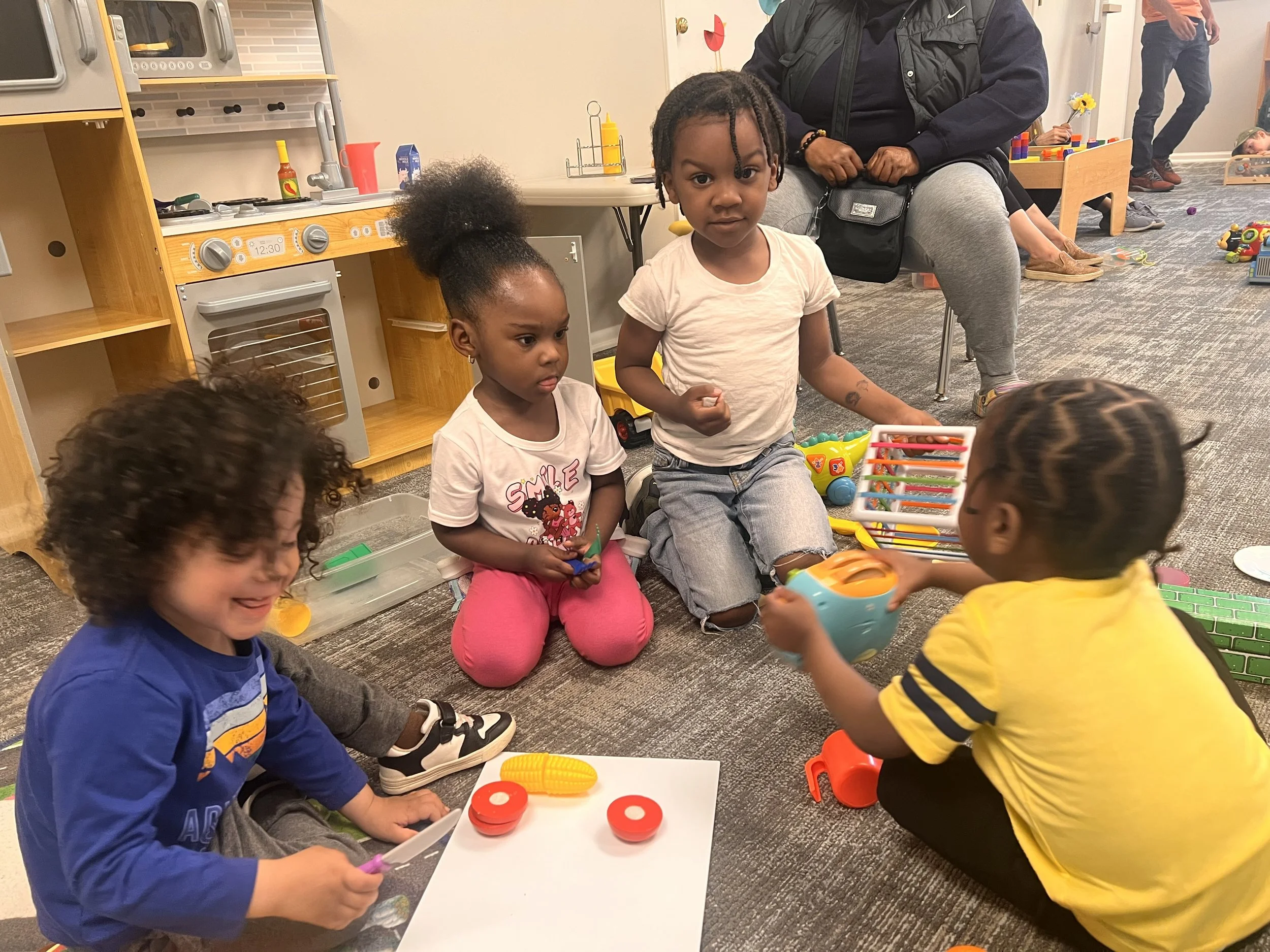 Children and an adult sitting and playing with toys in a classroom or play area.