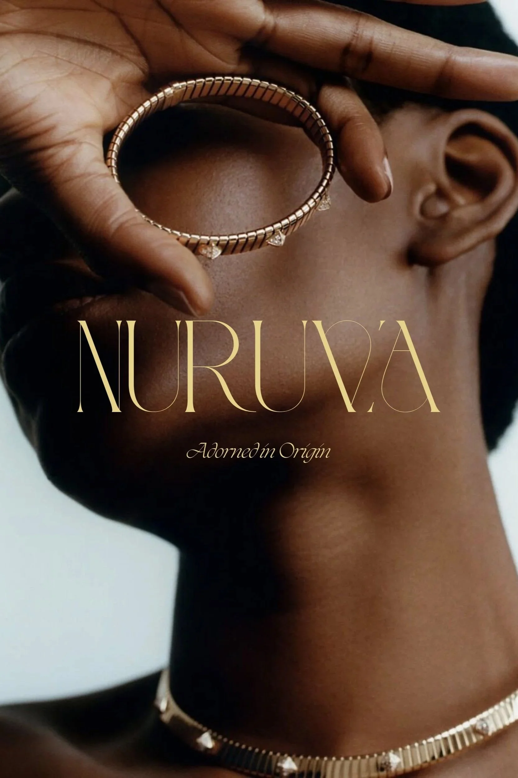 A woman with dark skin is holding a gold bracelet in front of her face, covering her eyes. She is also wearing a gold choker necklace with triangular details. The text on the image reads 'NURU'A' and 'Adorned in Origin'.