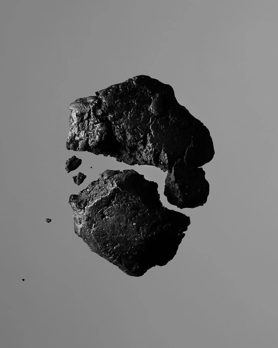 Black rock fragments on a reflective surface creating a mirror image, with a plain gray background.