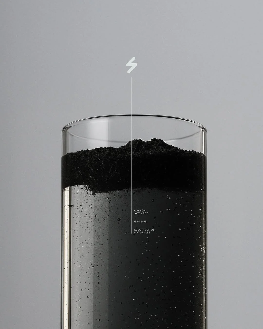 A clear glass contains a layered black powder with labels from top to bottom: activated charcoal, ginseng, natural electrolytes, against a gray background.