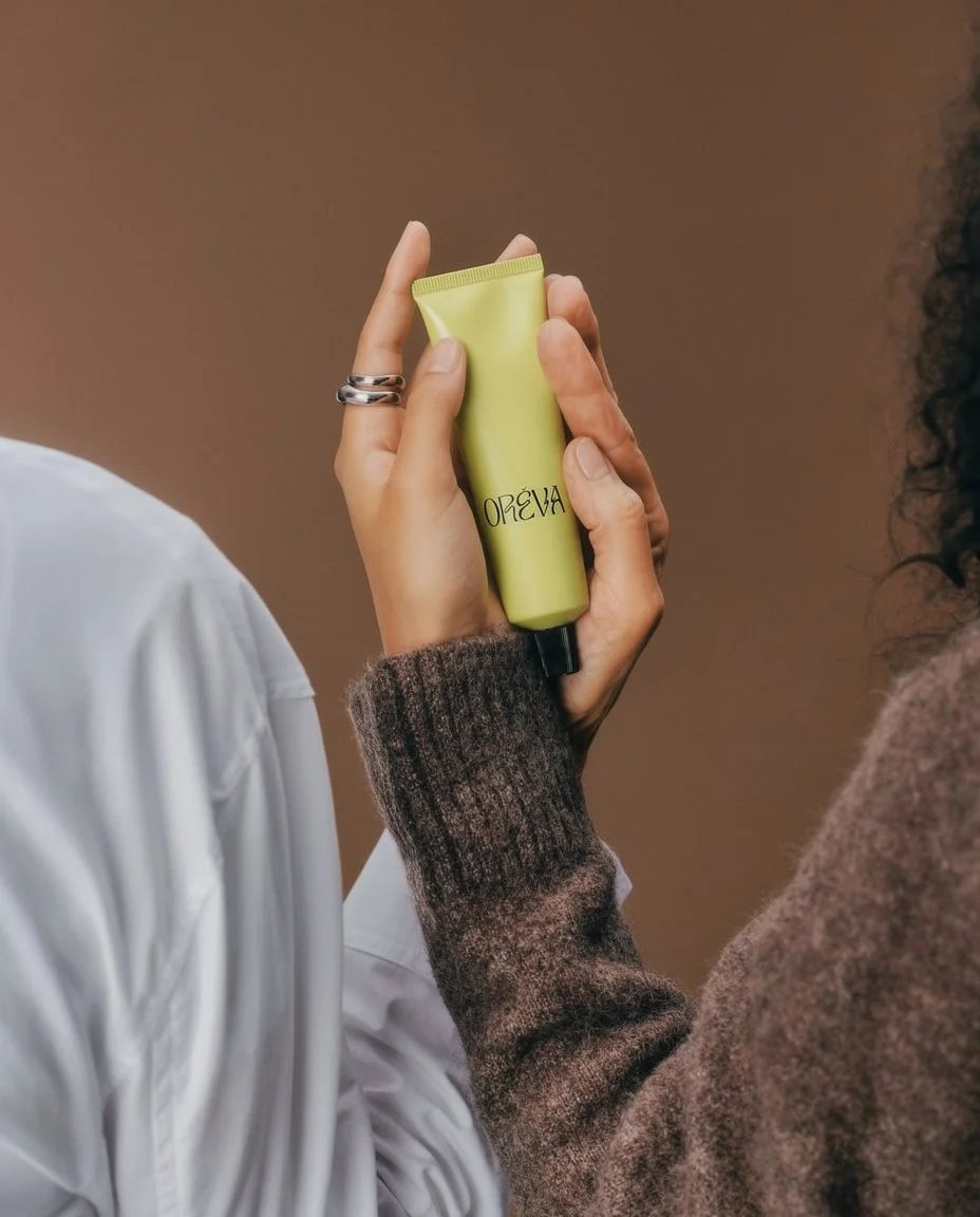 Close-up of a person holding a yellow tube of skincare product labeled 'OREVA' with another person in the background.