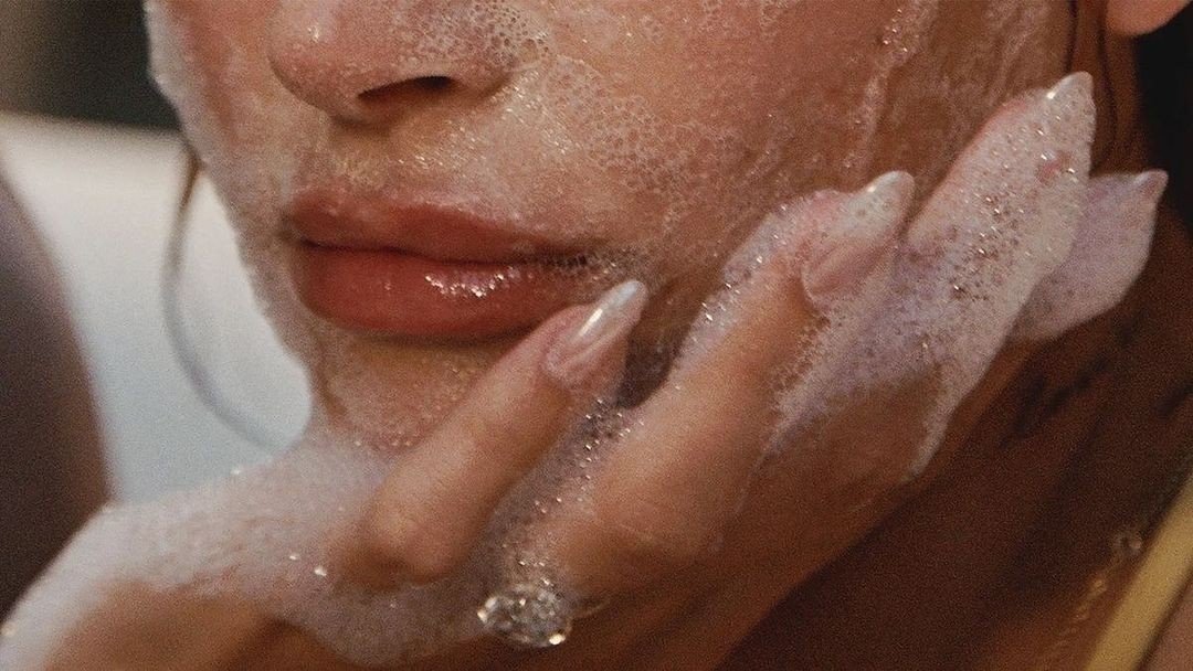 Close-up of a woman's face and hand with soap suds, touching her chin and lips.