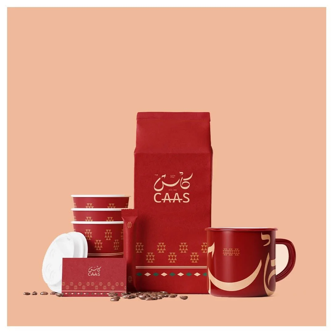 Coffee gift set with CAAS branding, including a red bag of coffee, a red mug, a red coffee capsule, and four disposable cups with CAAS logo, decorated in red and beige patterns, set against a peach background.