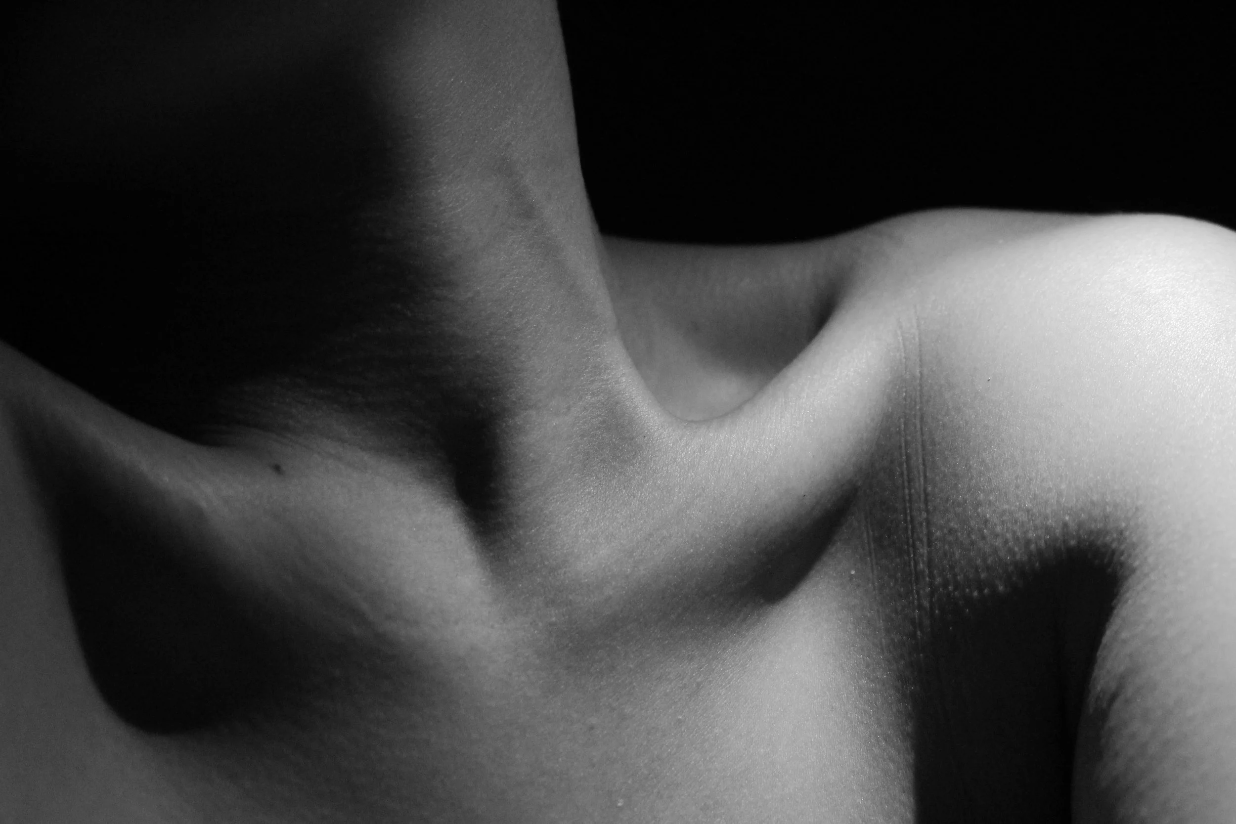 Close-up black and white photo of a person's back, focusing on shoulder blades and upper back, with smooth skin and muscle contours visible.