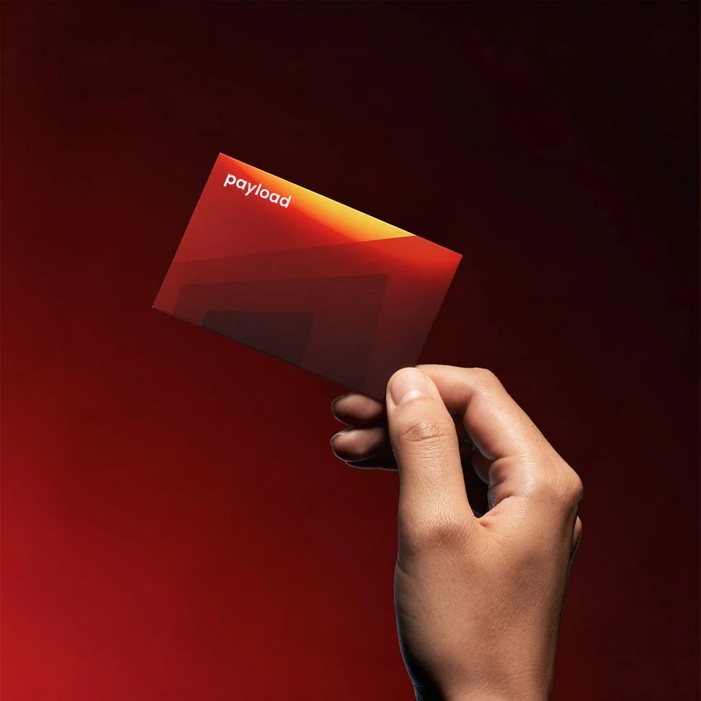 A hand holding a red and orange gradient card with the word "payload" written on it, against a dark red background.